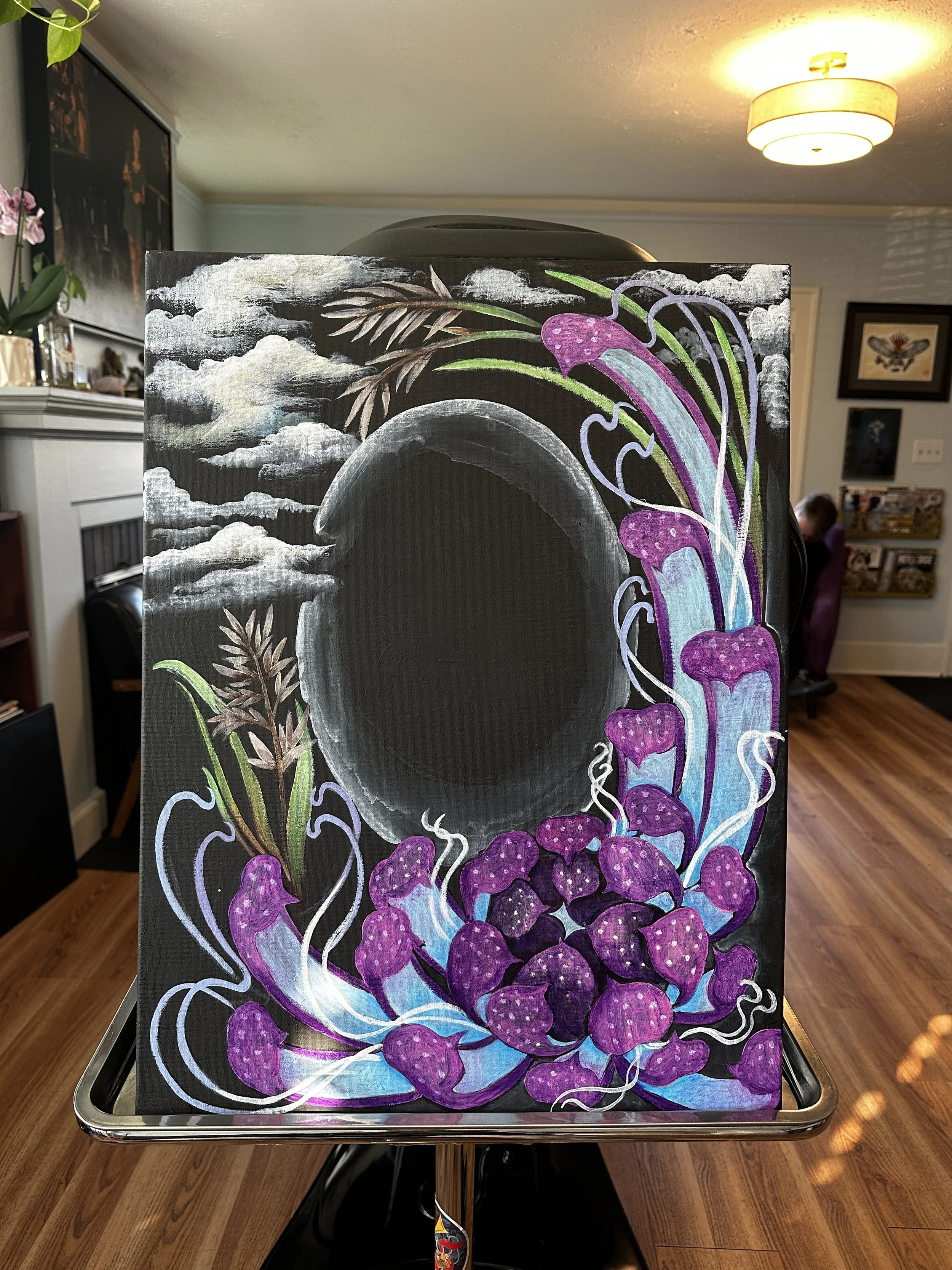 A colorful painting on a canvas features a waterfall with purple mushrooms and green plants, set against a cloudy sky background. The artwork is placed on a black easel in a cozy indoor setting.