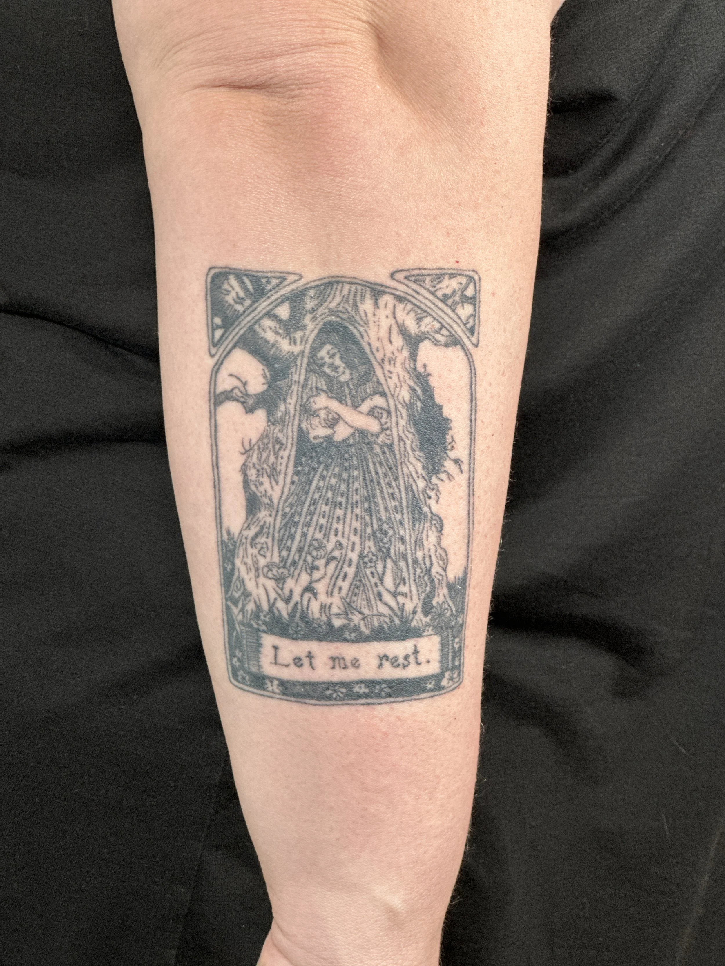 Tattoo of a tree with a person sitting inside a hollow, with the words "Let me rest." written below on the person's arm.