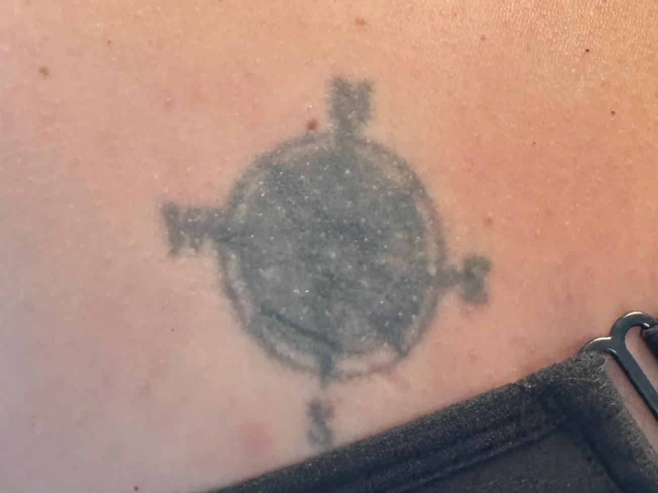 Close-up of a small, black ink tattoo of a simple spaceship or UFO design on skin.