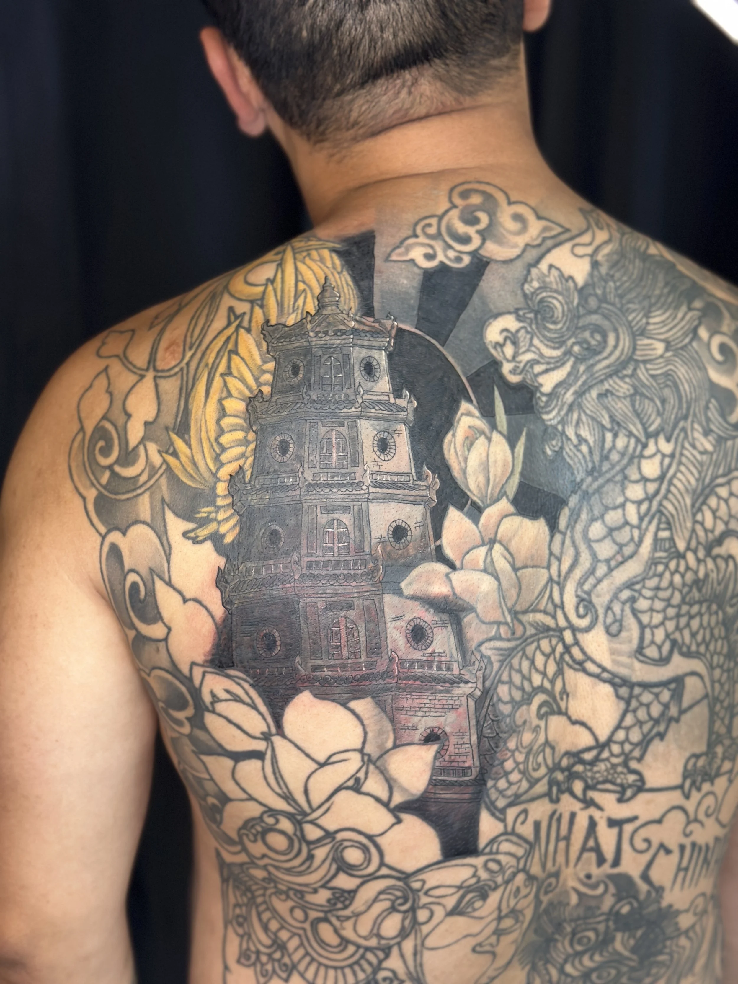 Tattoo of a traditional Asian pagoda-style building on a man's shoulder and upper chest, with additional cloud and dragon designs.