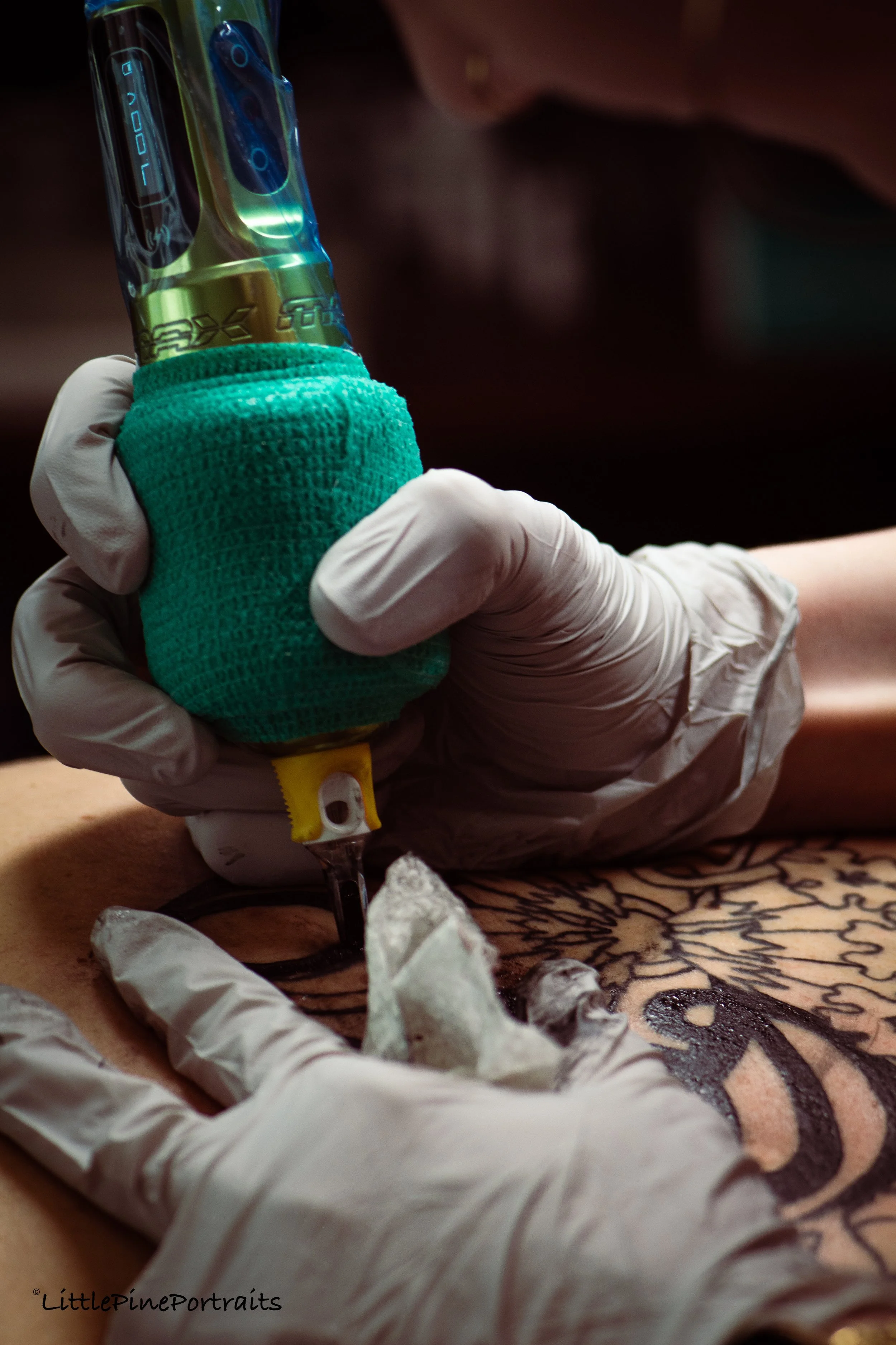 Close-up of a person's hand wearing a white glove holding a medical IV drip tube, with a green foam grip, against a dark background.