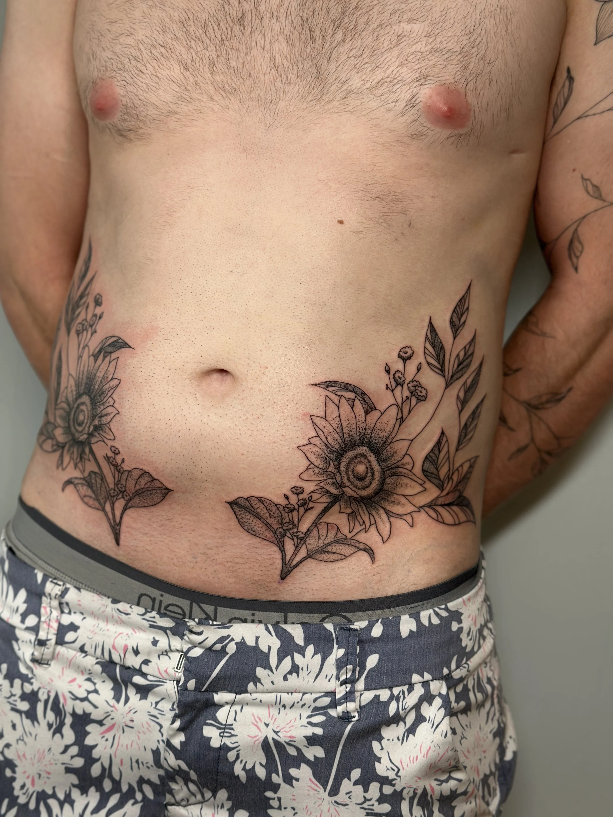 Close-up of a man's torso with floral tattoo designs across the stomach and side.