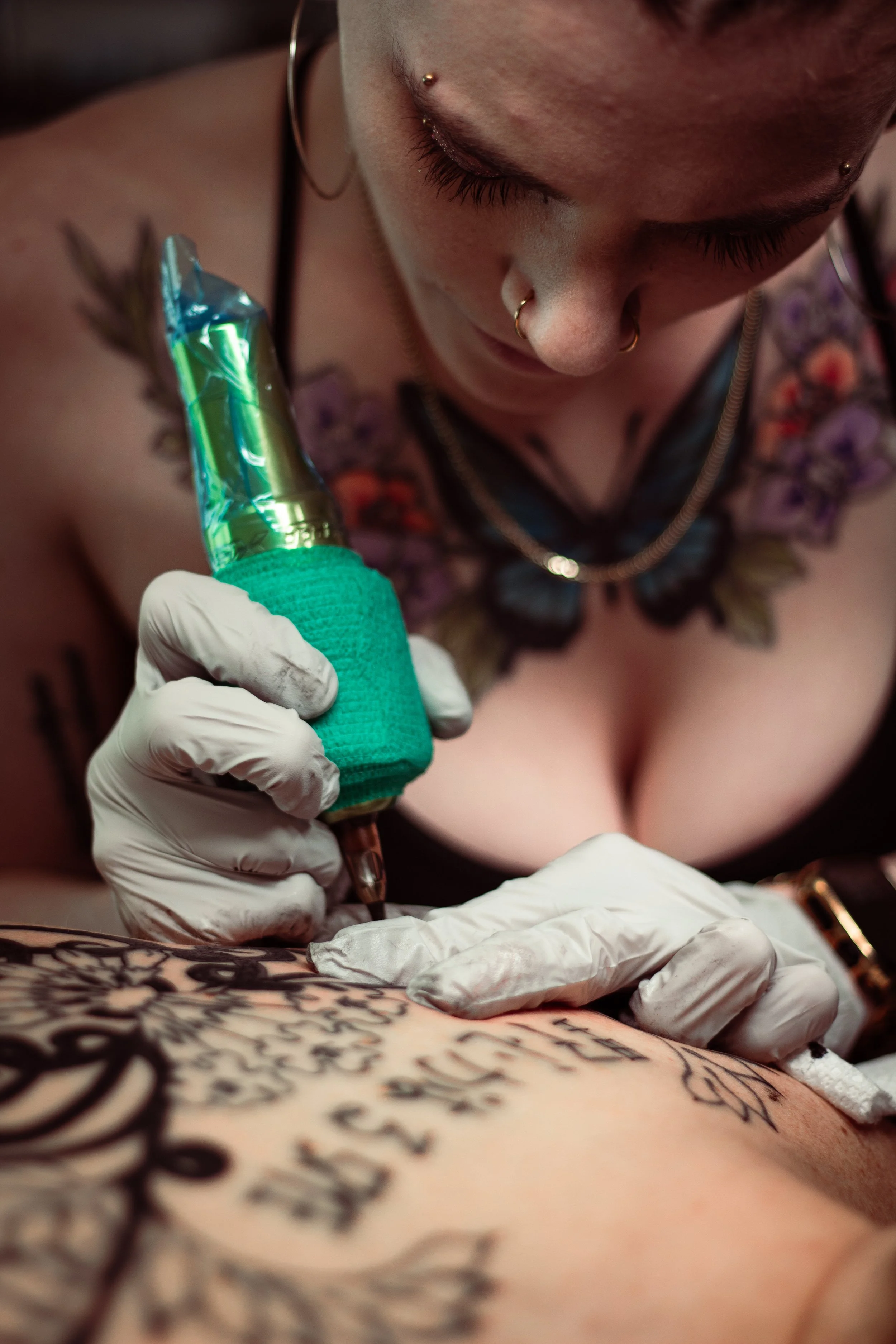 A person with tattoos receiving a tattoo on their skin from an artist using a tattoo machine.