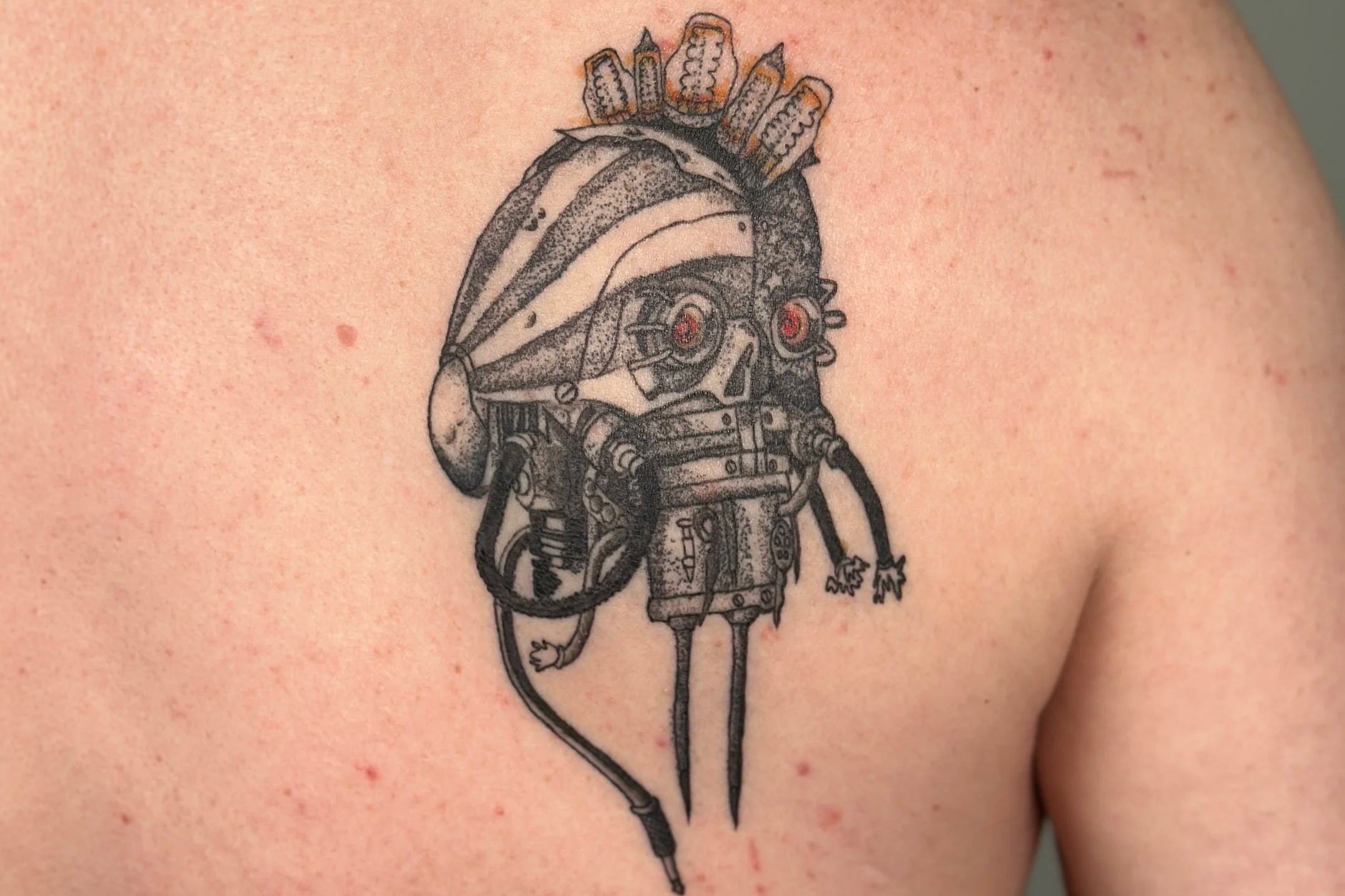 Tattoo of a detailed, black and gray mechanical mouse with a tribal headdress, located on a person's shoulder.