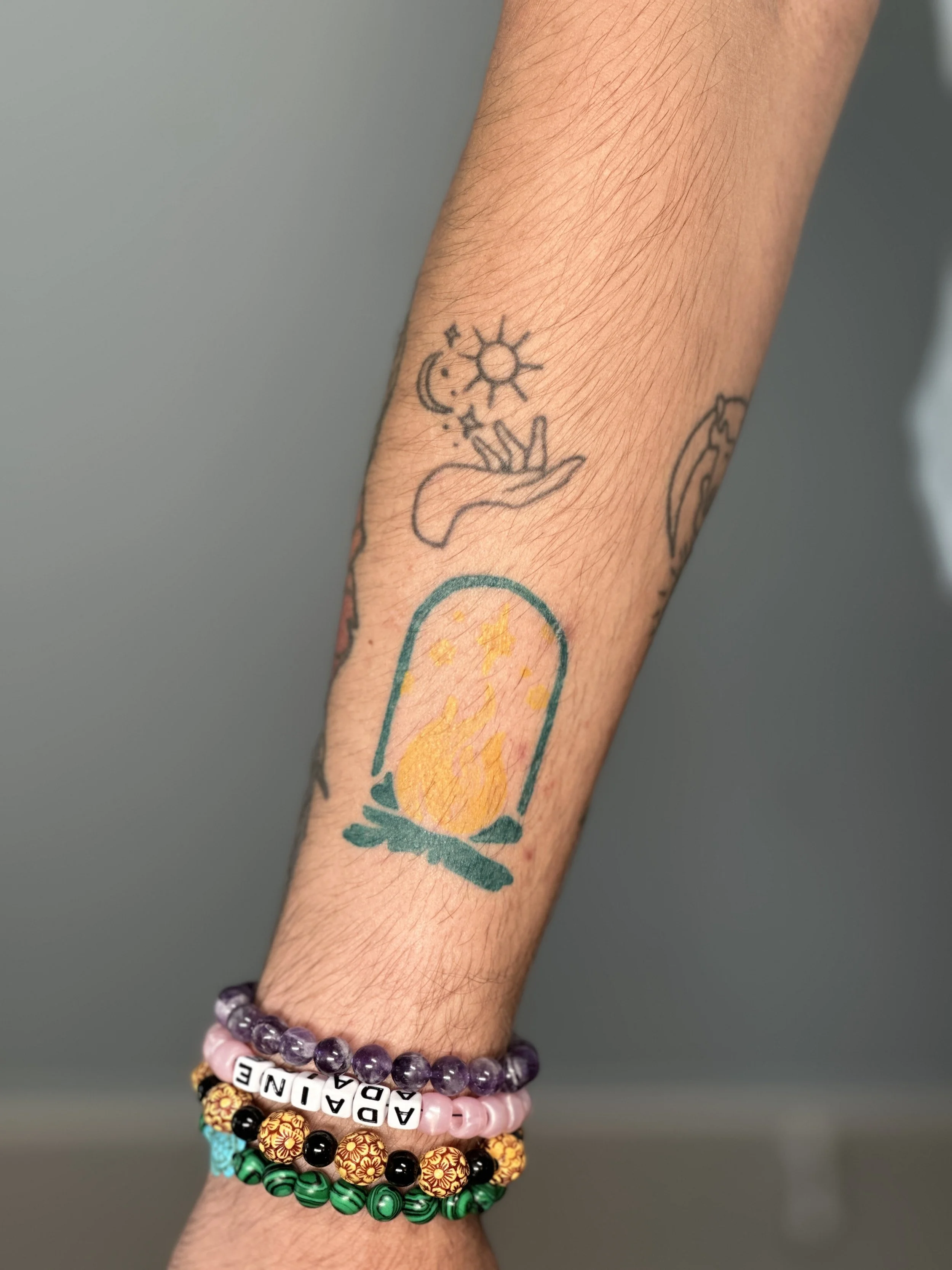 A person's arm with multiple colorful bracelets and a small tattoo of a hand with celestial symbols above it.