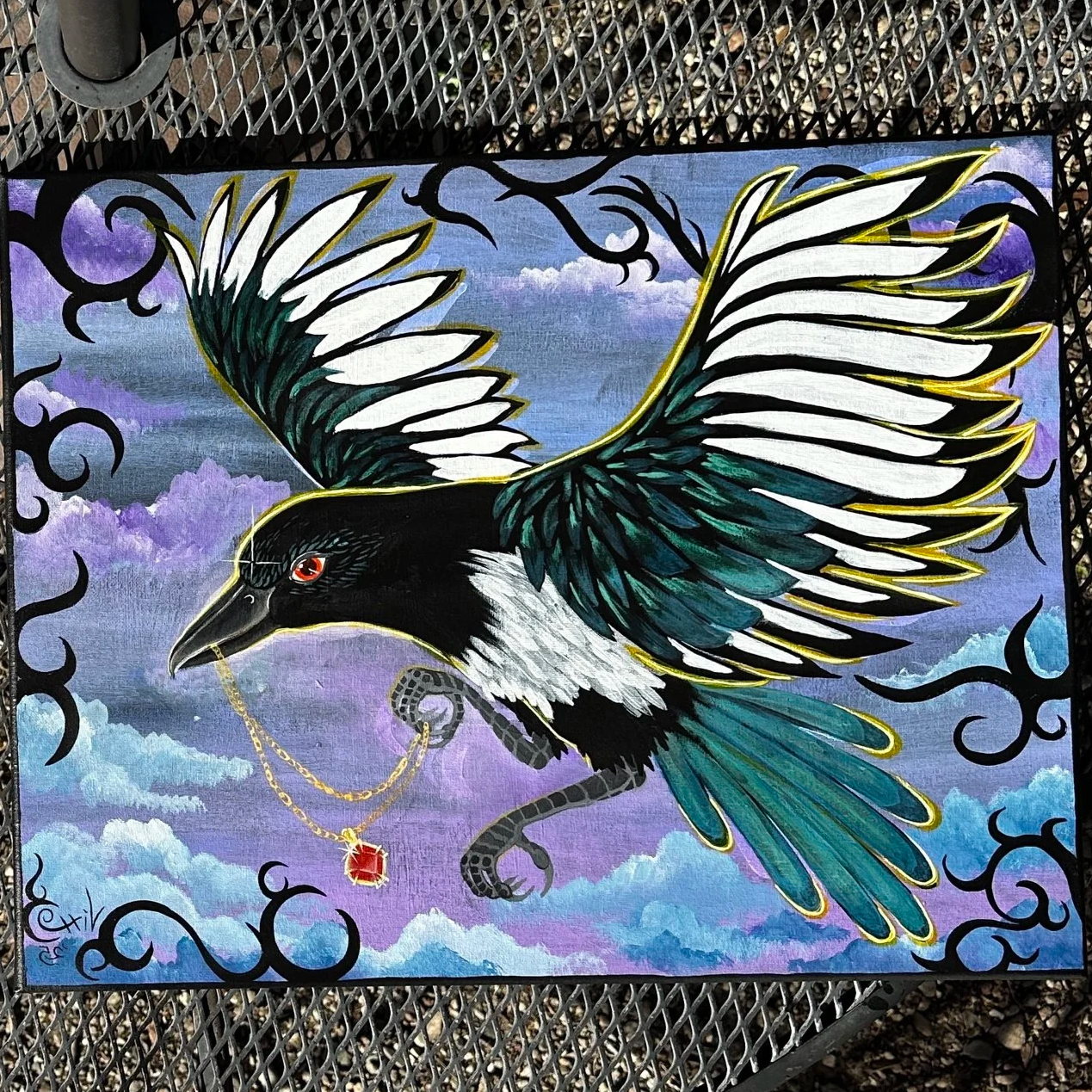 A mural of a black and white bird with green and blue wings flying against a cloudy sky background. The bird is holding a gold chain with a red gemstone pendant in its beak.