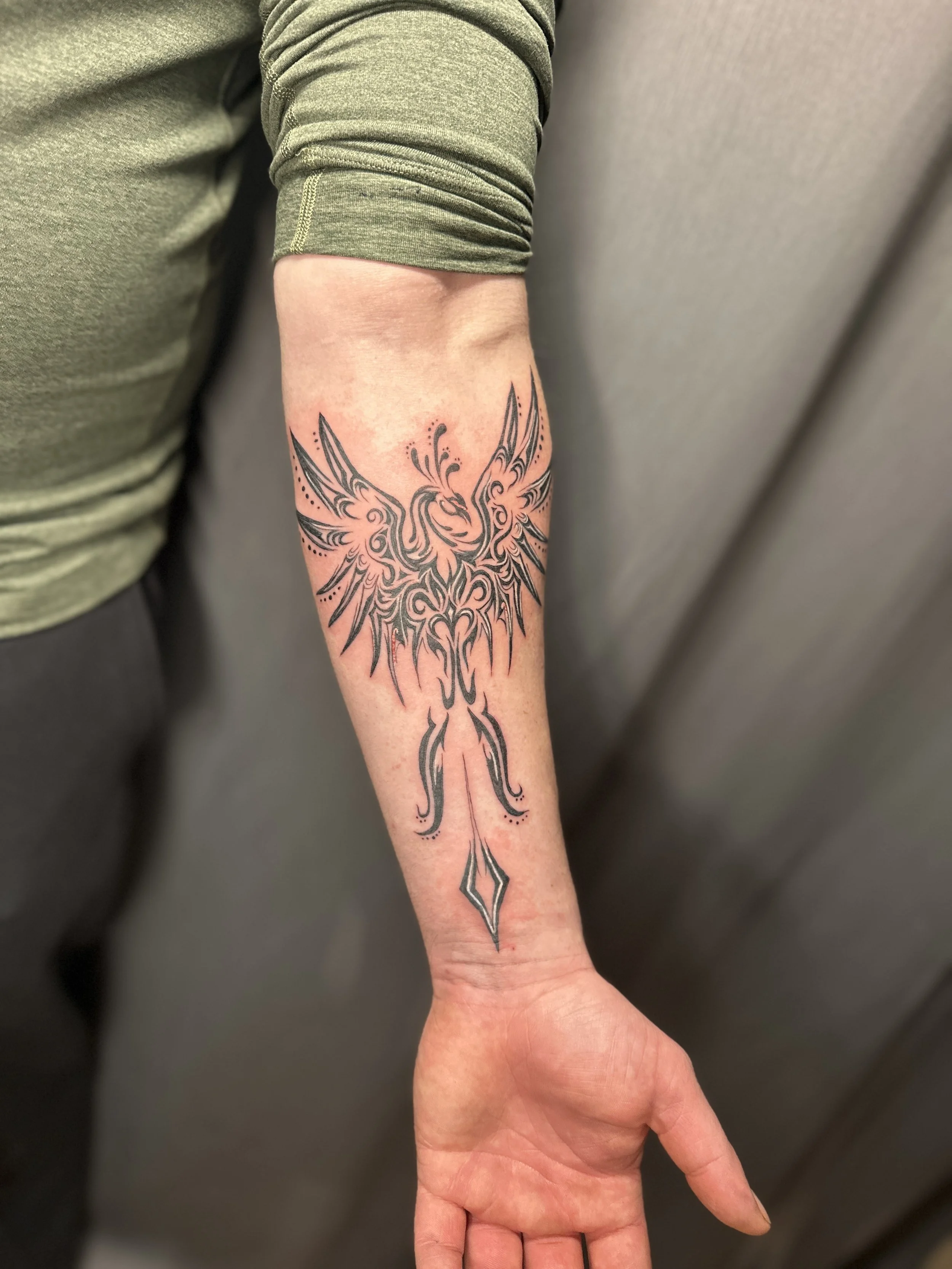 Tattoo of a stylized, symmetrical creature with wings and intricate details on a person's forearm.