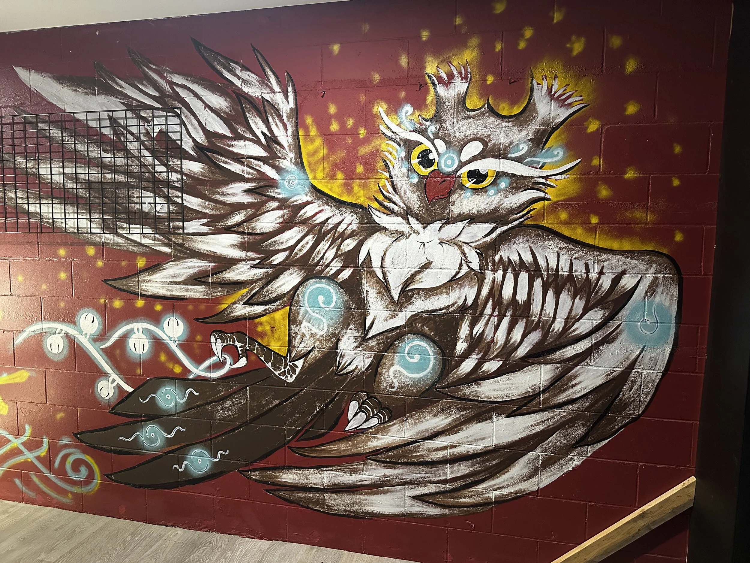 Graffiti mural of a mystical, stylized eagle with large wings, vibrant eyes, and decorative elements on a red wall.