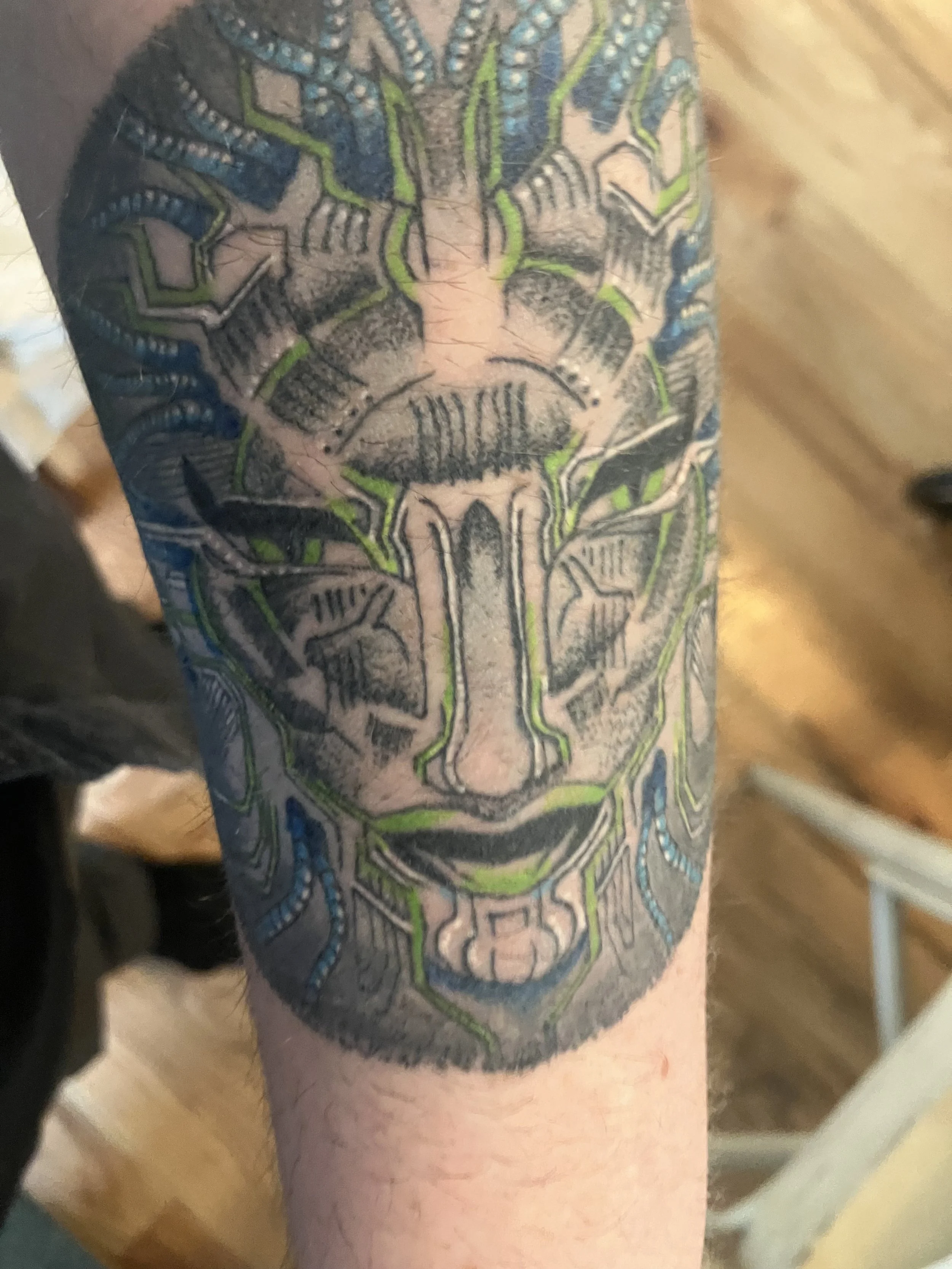 A detailed tattoo of a scarecrow's face on a person's forearm, with intricate lines, colors, and shading.