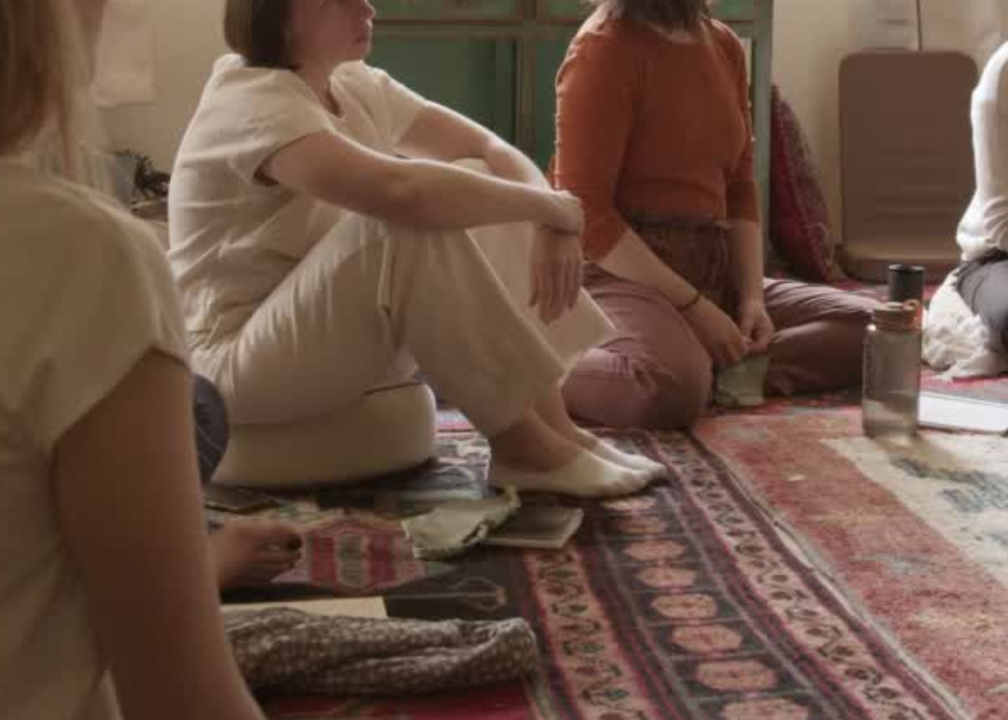 People sitting on a patterned rug in a room, engaging in a group activity or discussion.