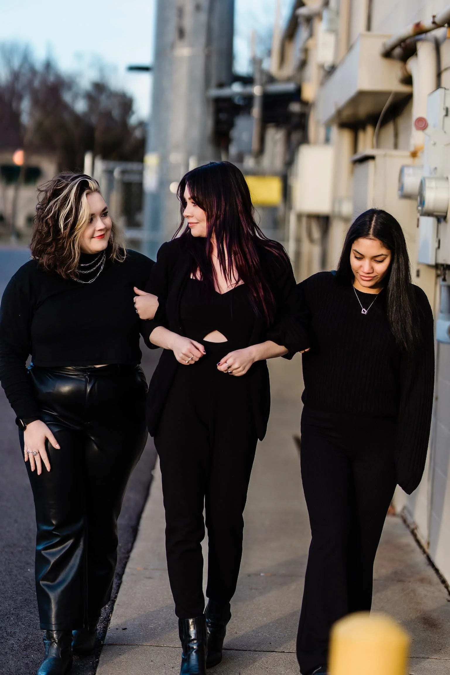Three women walking together on a city street, enjoying each other's company. The women are dressed in black and seem to have fashion-forward styles.