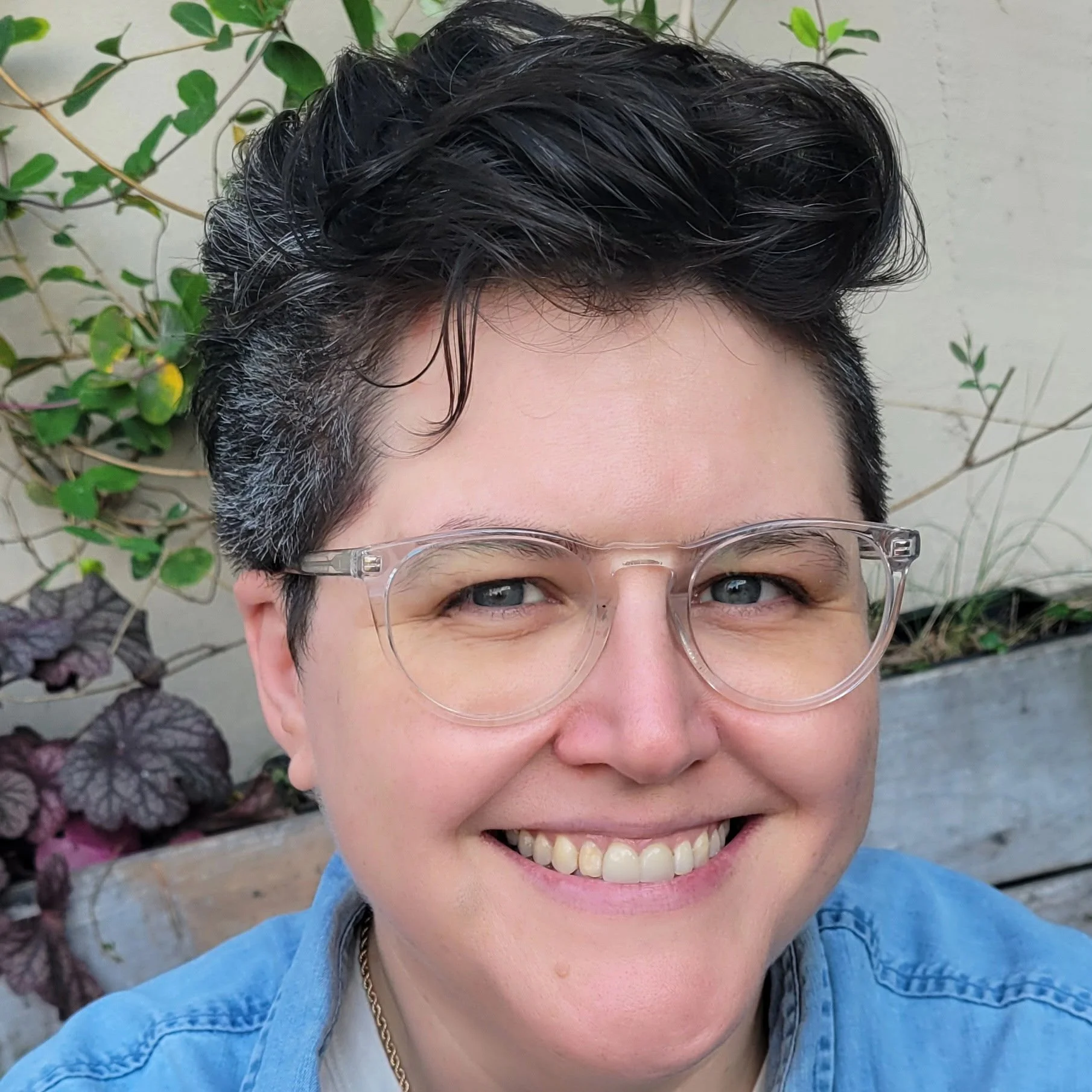 Joey, a white nonbinary person with dark curly hair and glasses, smiling at the camera