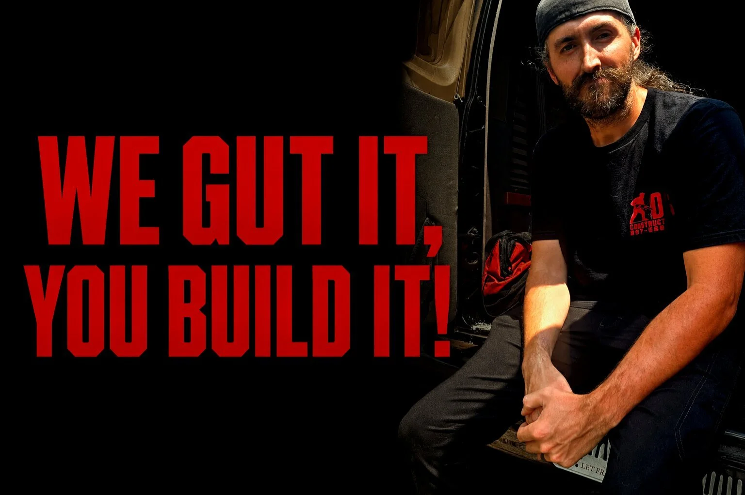 A man with long hair and a beard, wearing a black cap and black t-shirt, crouching near an open vehicle door. The shirt has a red logo for a construction company. Next to him, bold red text on a black background reads: 'WE GOT IT, YOU BUILT IT!'.