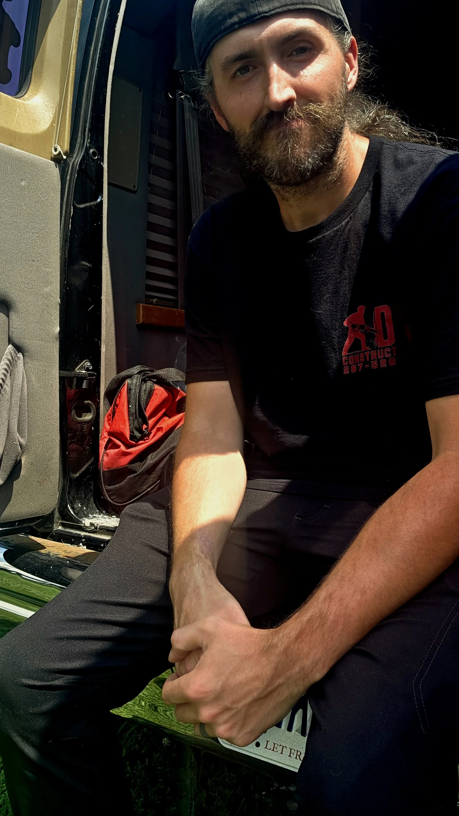 photo of owner vincent leary, bearded man with a mustache in a black hat sitting in a work van with tools. dvs construction work van and t-shirt