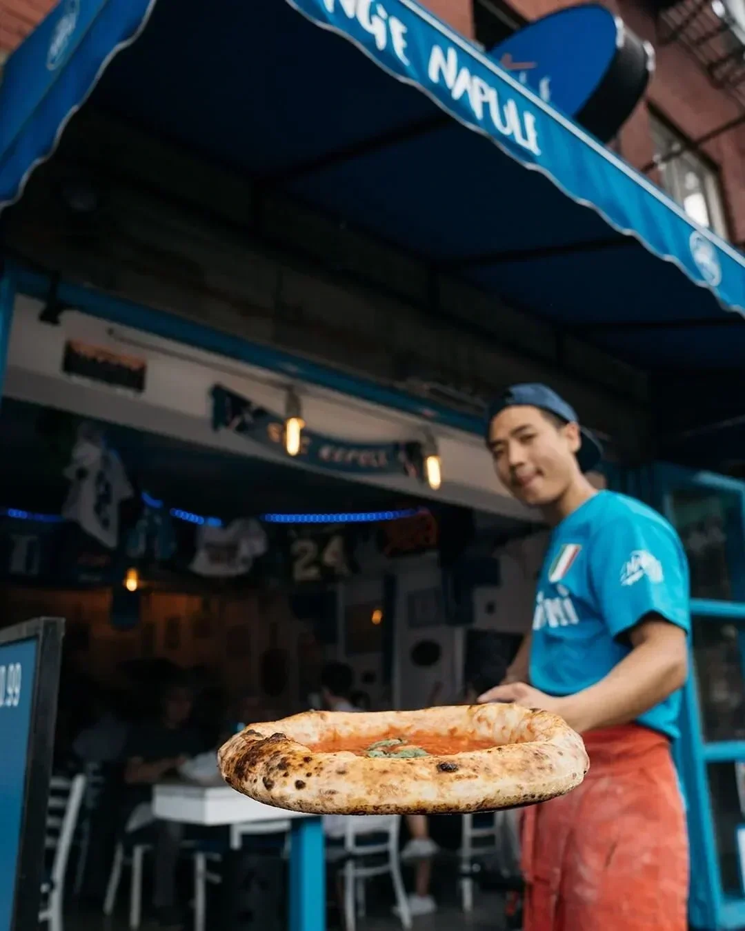 Giggino holding a marguerita pizza to the screen