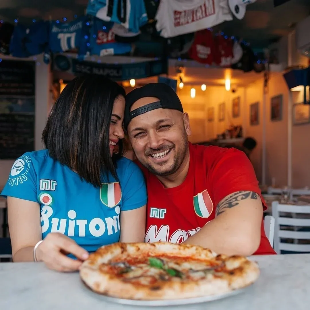 Austria and Ciro close together and smiling with a margherita pizza