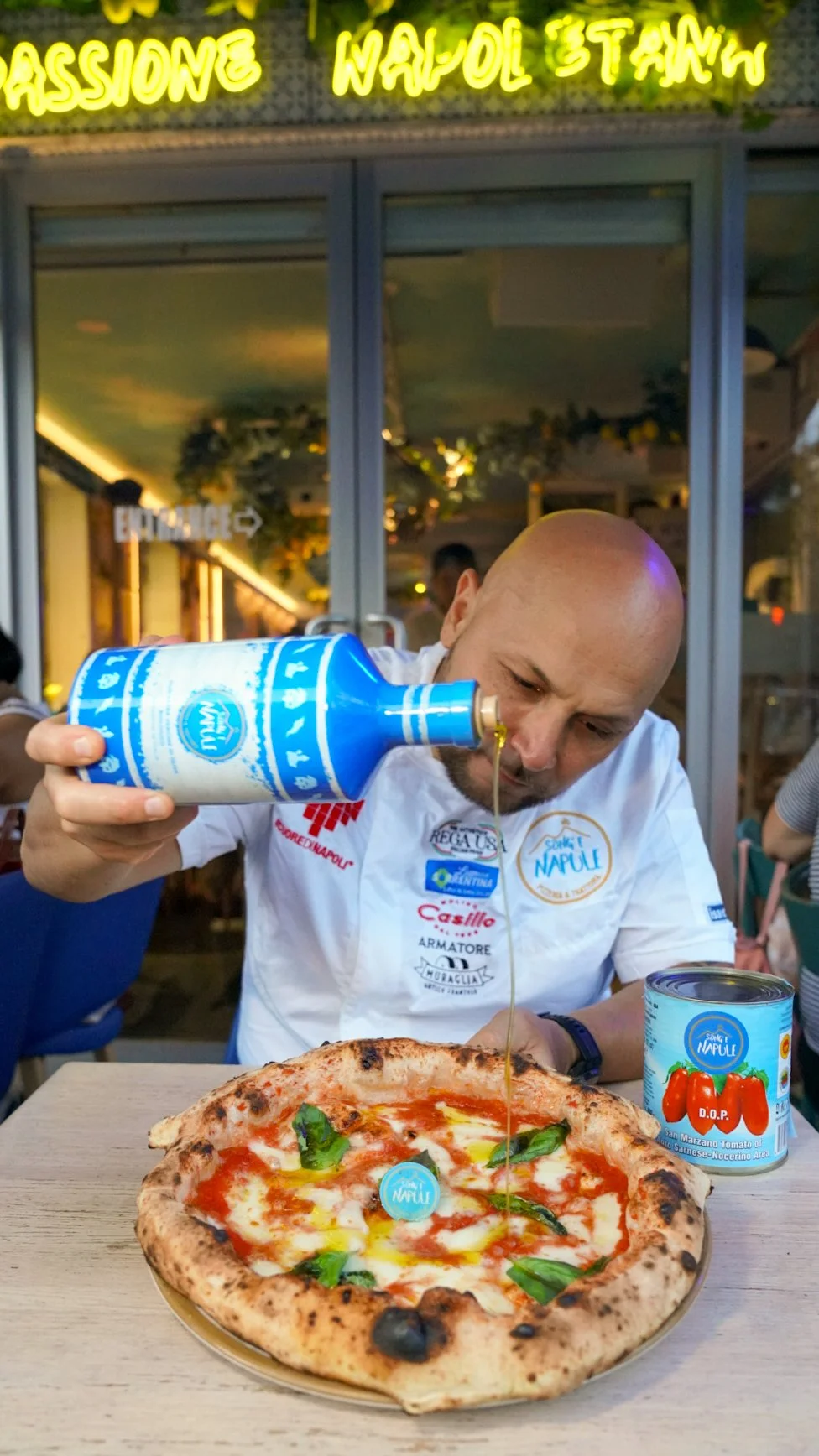 Ciro pouring Extra Virgin Olive Oil on a margherita pizza
