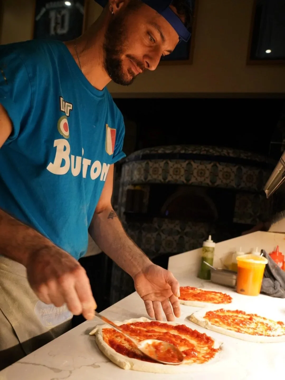 Pizzaiolo spreading tomato sauce to pizza dough