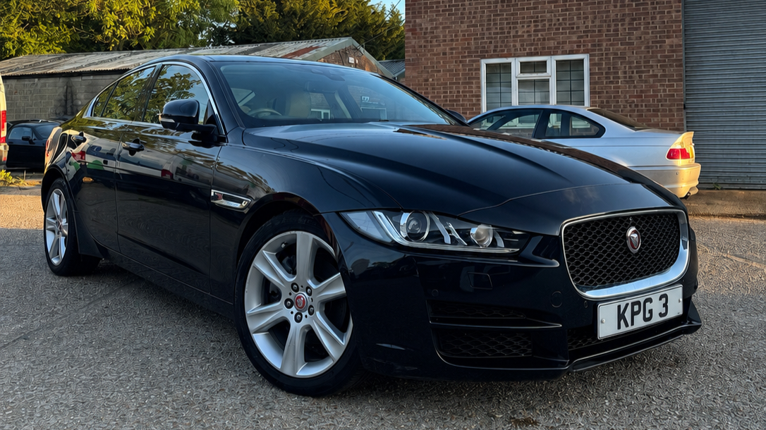 Black Jaguar sedan parked on a gravel lot with other cars and buildings in the background.