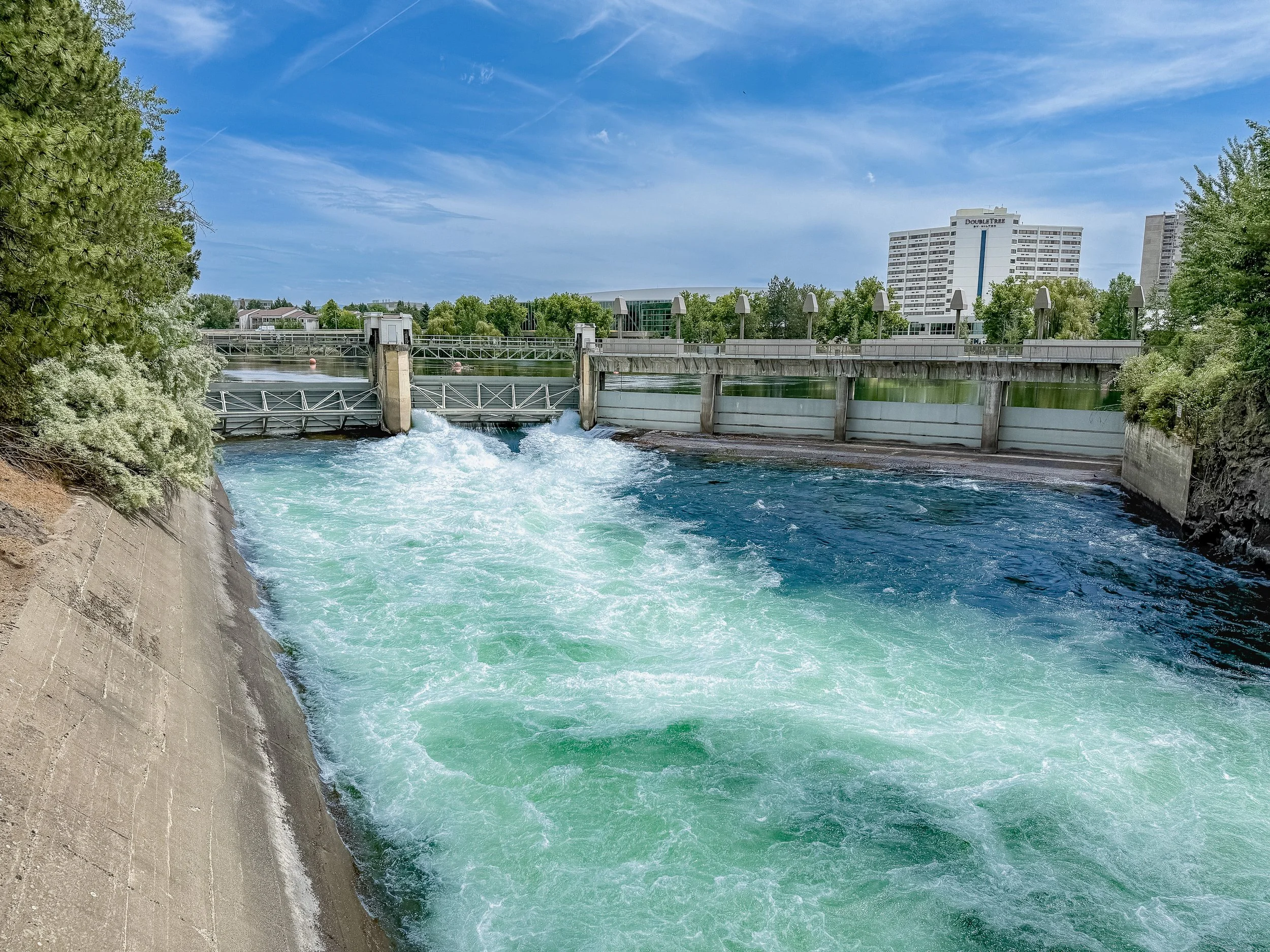 The gated spillway at Upper Falls Dam releases water toward the falls below. From this angle, the Spokane River looks engineered and controlled; downstream, the same flow becomes the whitewater seen from Riverfront Park’s pedestrian bridges.