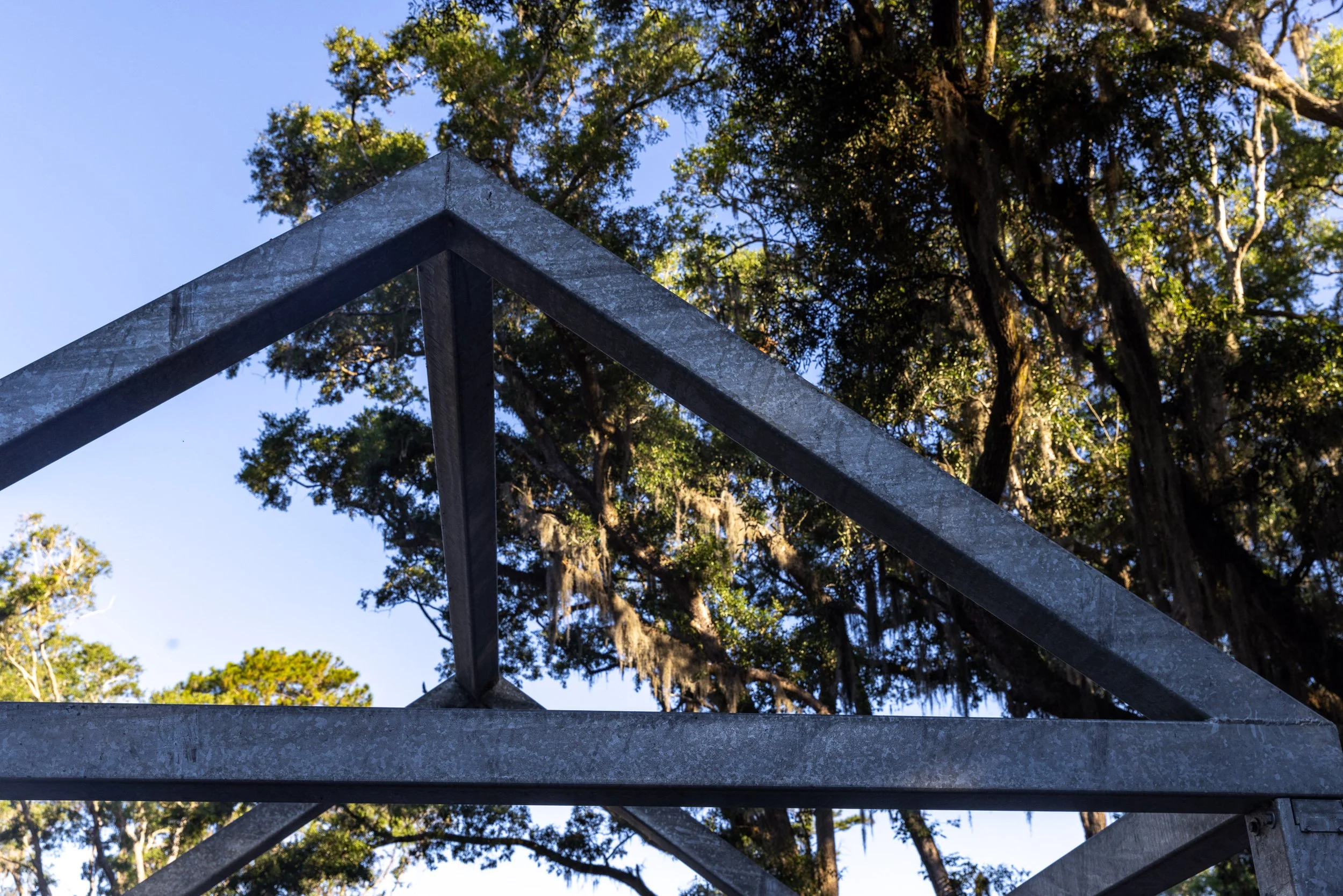 Steel rooflines frame live oaks and Spanish moss at Historic Mitchelville Freedom Park. The Ghosted Structures make absence visible, using little more than an outline to ask what stood here, who built it, and why so much disappeared.