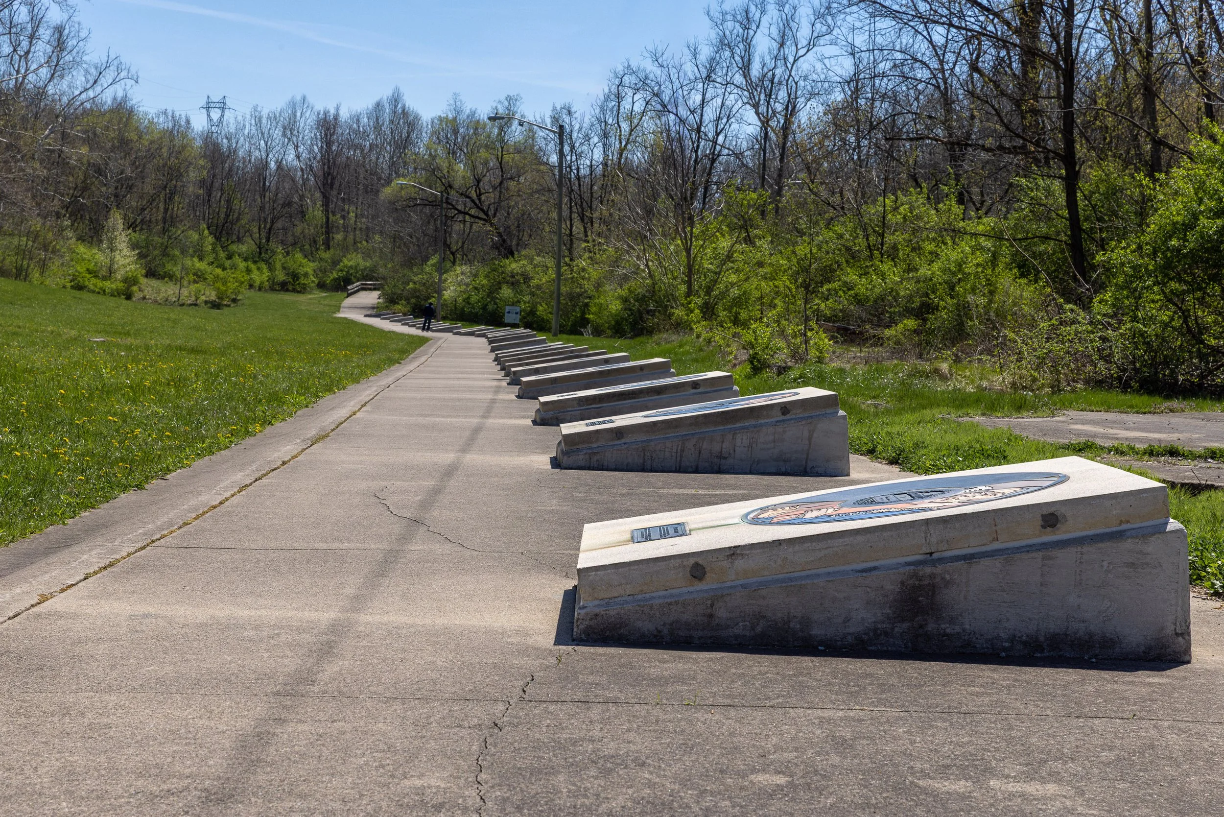Concrete record markers follow a curving path through the former Starr Piano grounds. Each one names an artist recorded by Gennett, turning an emptied industrial landscape into a physical catalog of early American sound.