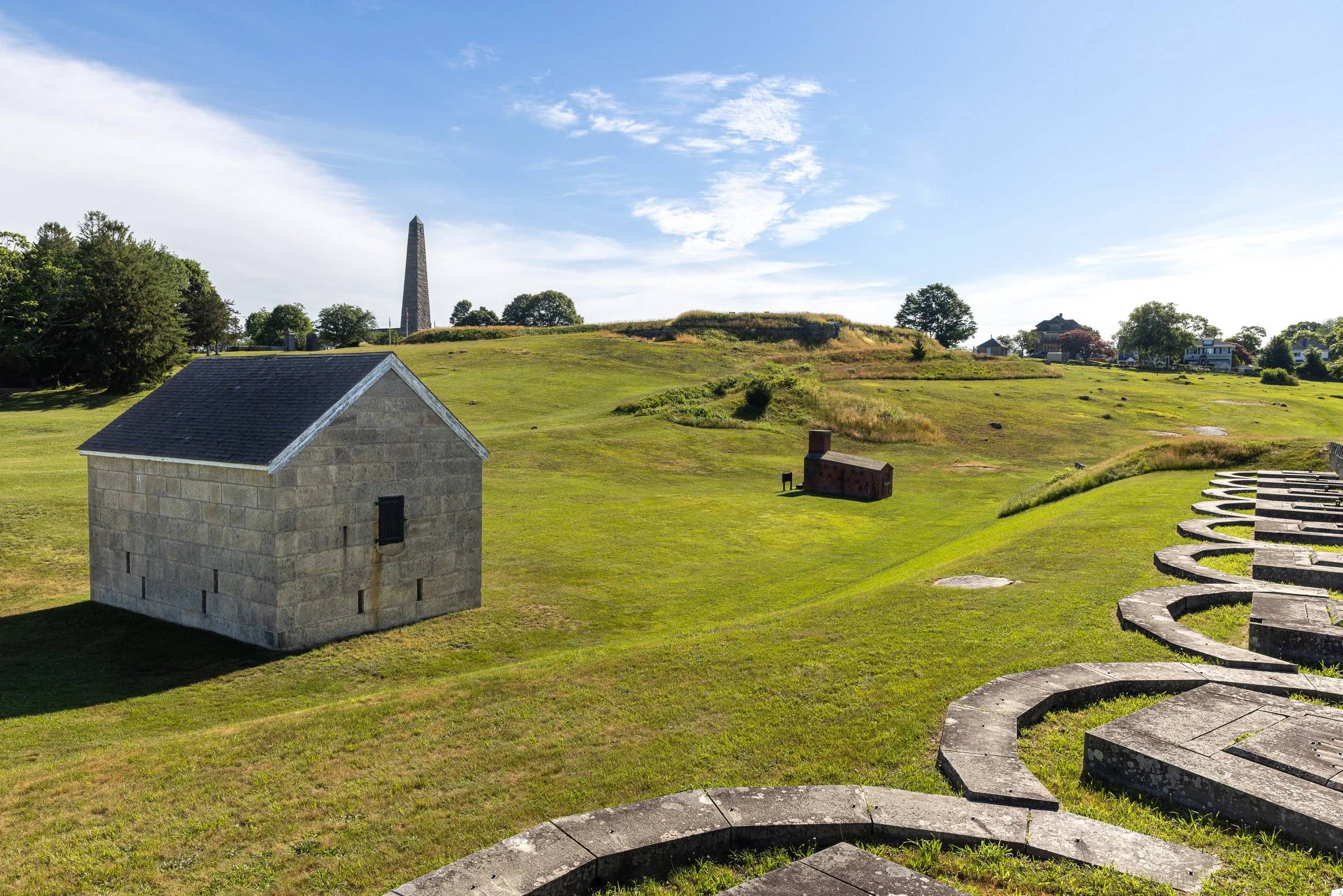 A stone powder magazine, brick shot furnace, grassy earthworks, and the Groton Monument share Fort Griswold’s lower battery. The layered landscape reveals how this strategic hill continued to serve harbor defense and remembrance long after the Revolu