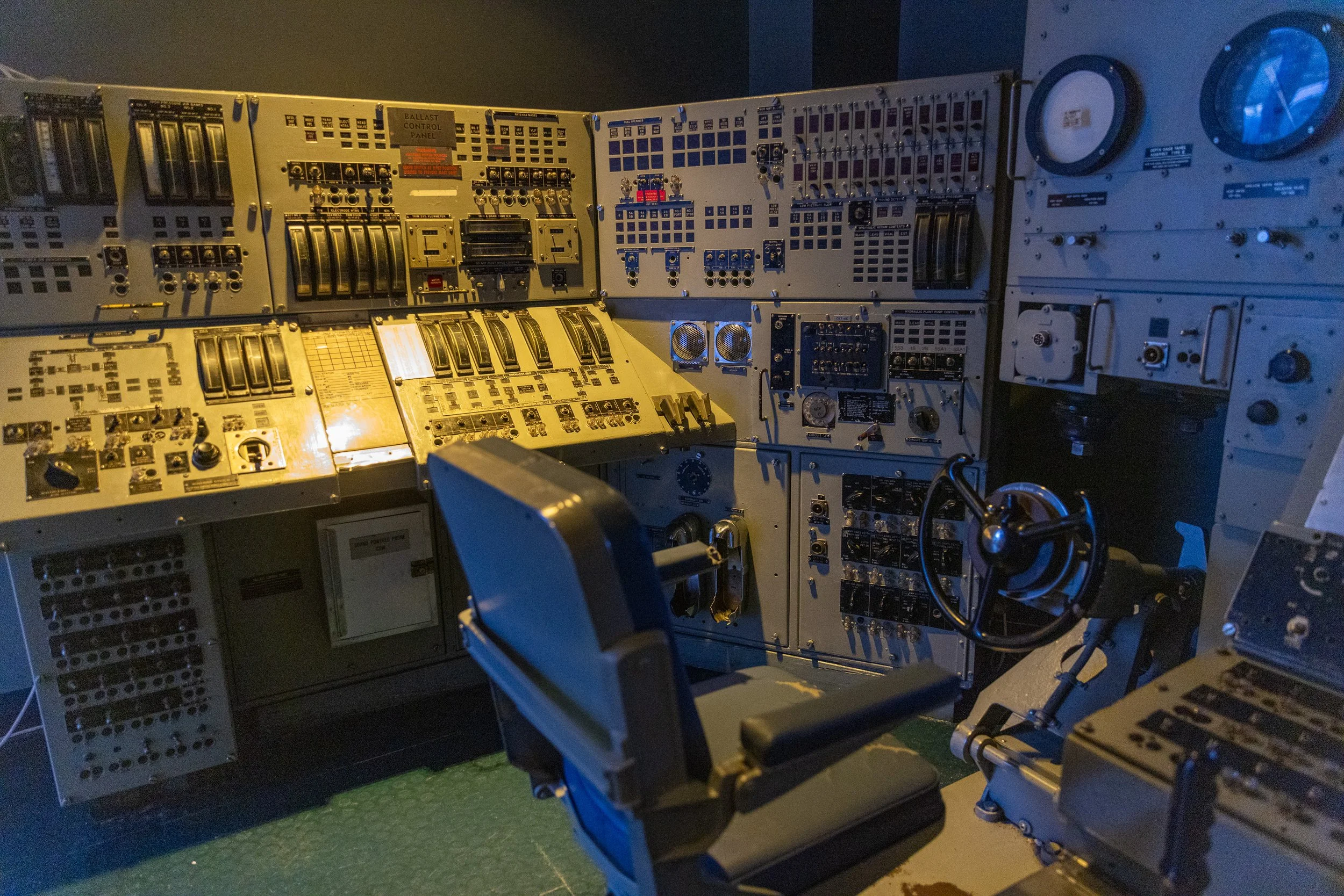 Recreated Cold War submarine control room filled with switches, gauges, control panels, wheels, and crew seats.