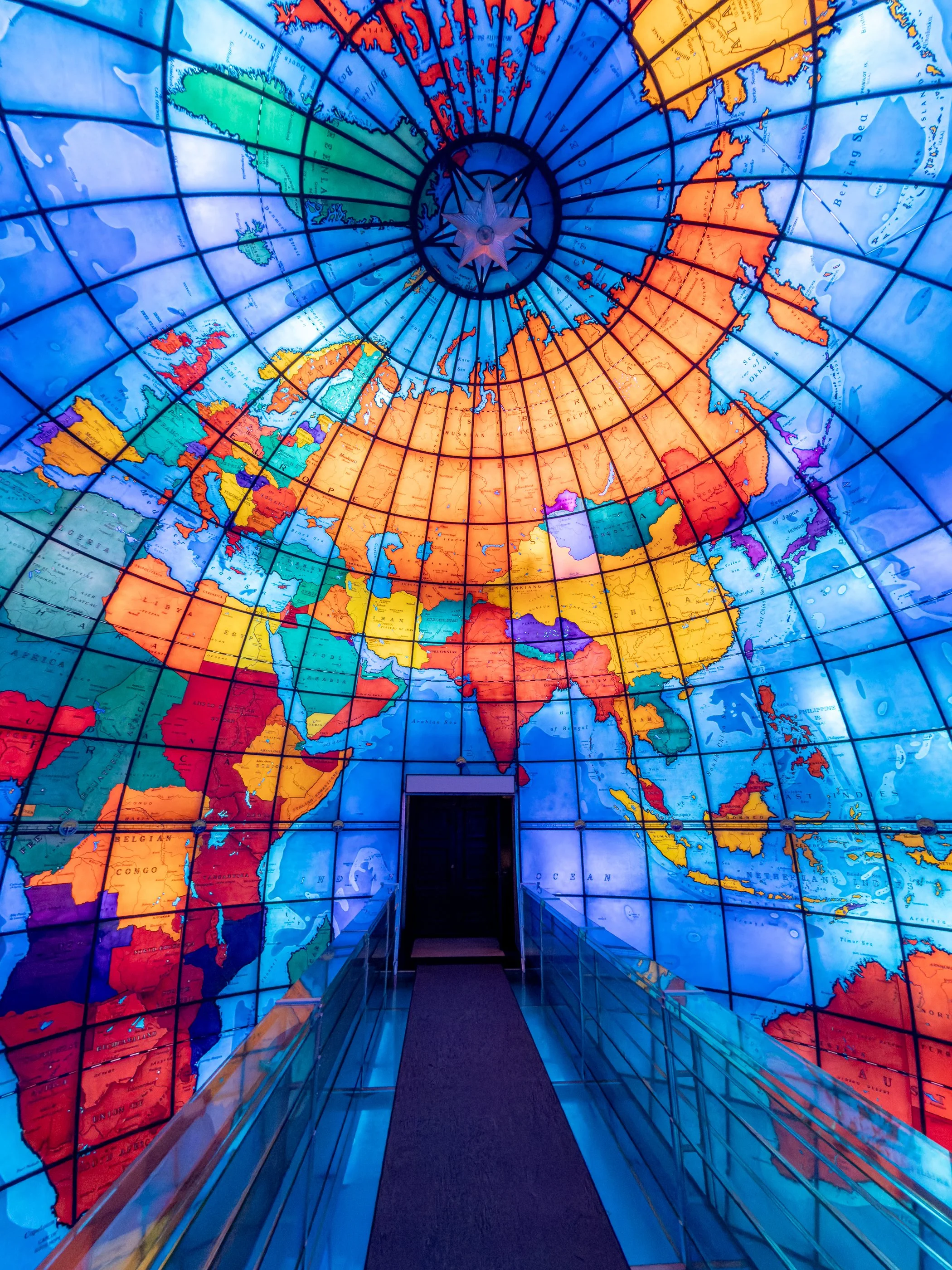 Inside Boston’s Mapparium globe, a glass bridge crosses the equator through the center of a thirty-foot sphere. Instead of looking down at a globe, visitors stand inside one—surrounded by 608 illuminated panels that turn the familiar shape of the wor