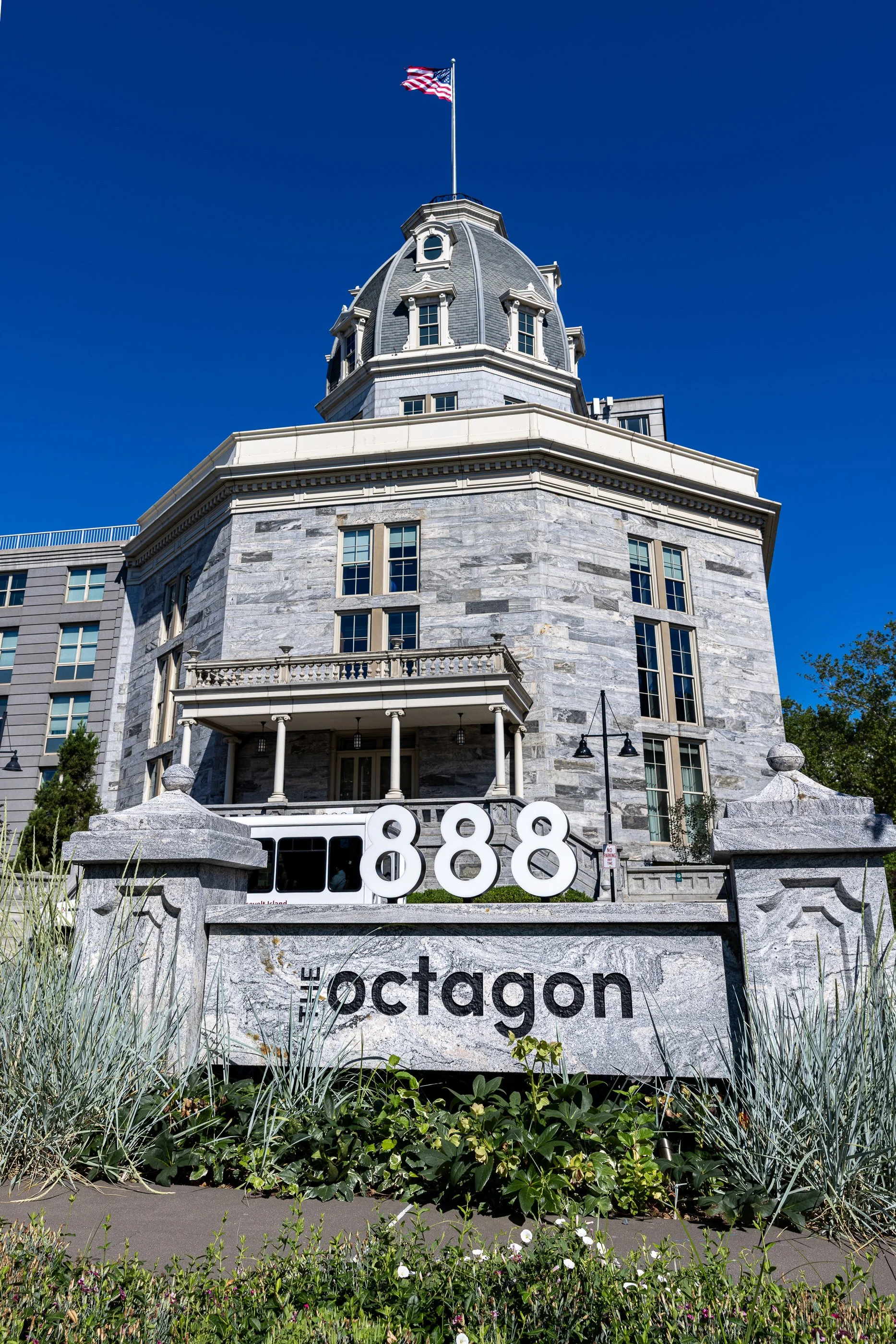 A gray stone tower rises behind an 888 Octagon sign at the entrance to The Octagon apartment complex on Roosevelt Island.