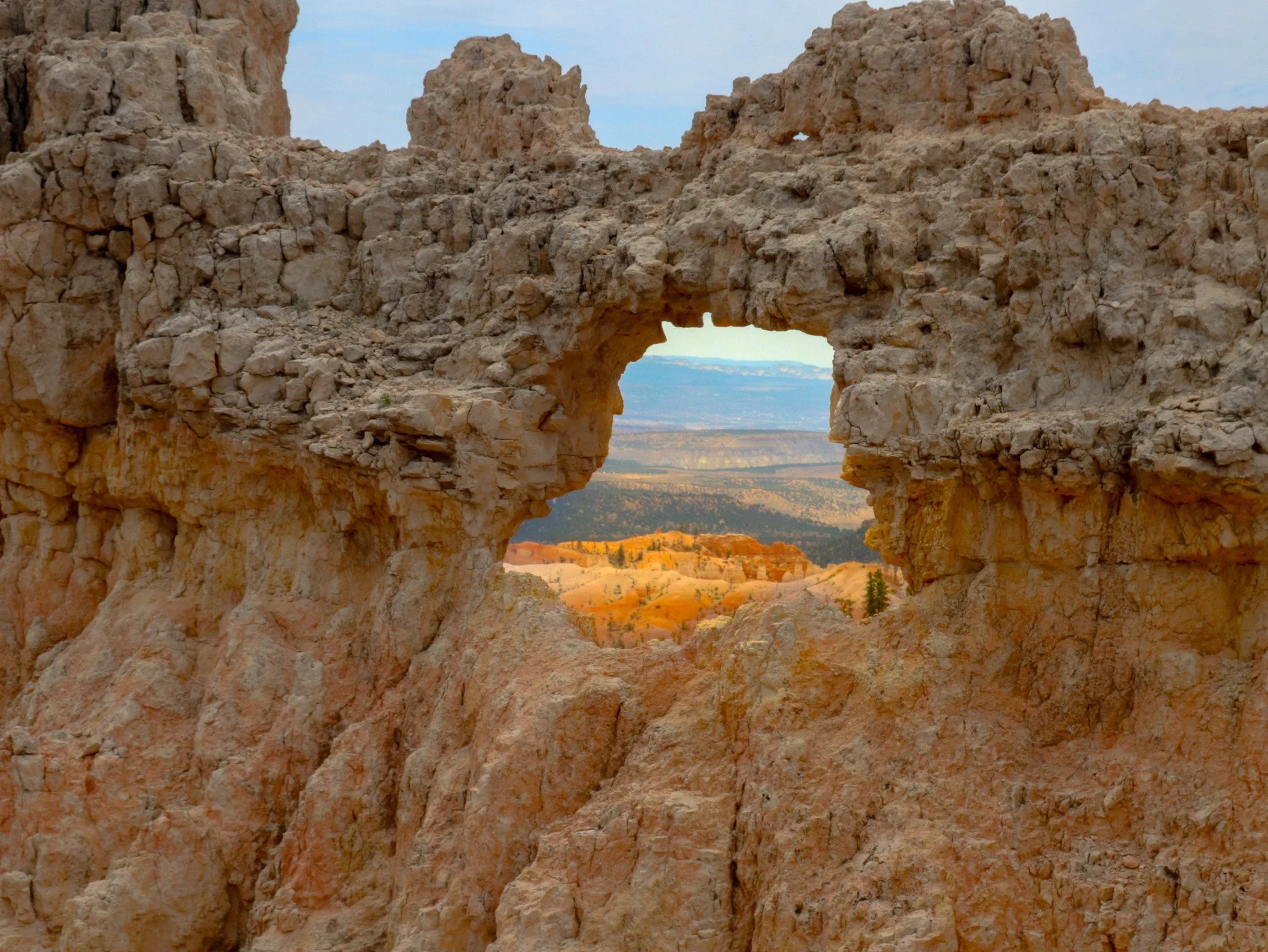 An opening in a pale, rough rock wall frames orange terrain and distant blue ridges.