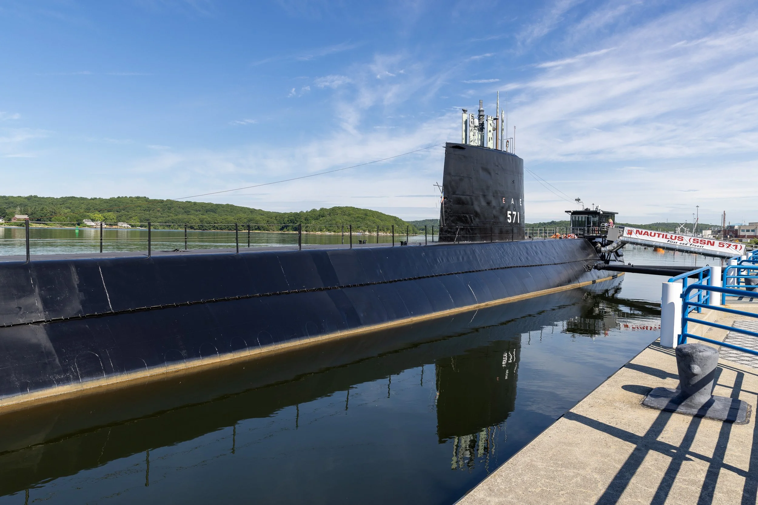 Wide side view of the black hull and sail of USS Nautilus moored at the Submarine Force Museum in Groton.