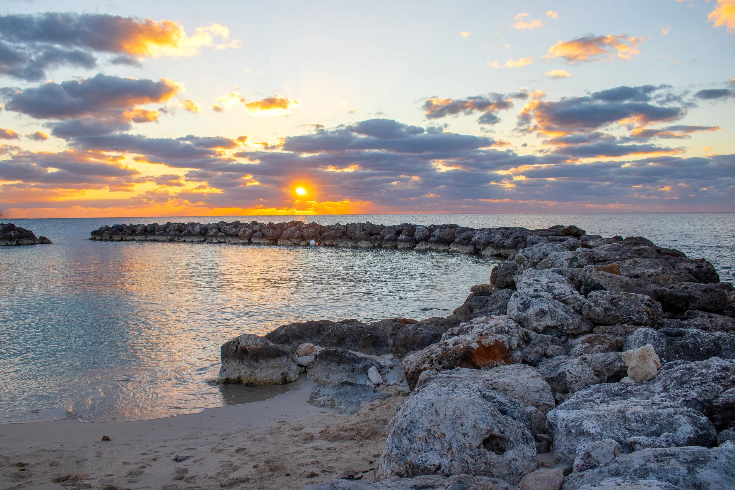 Sunset over the rocky breakwater and Caribbean Sea in Grand Cayman, Cayman Islands.