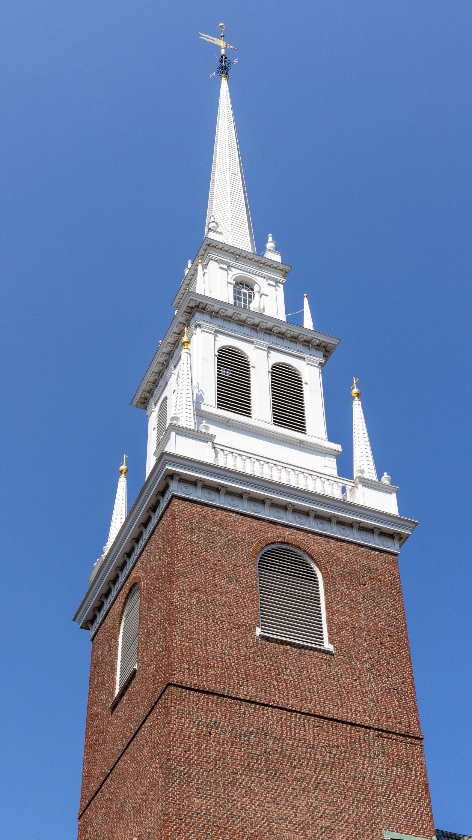 White steeple and red-brick bell tower of Old North Church against a clear blue sky.