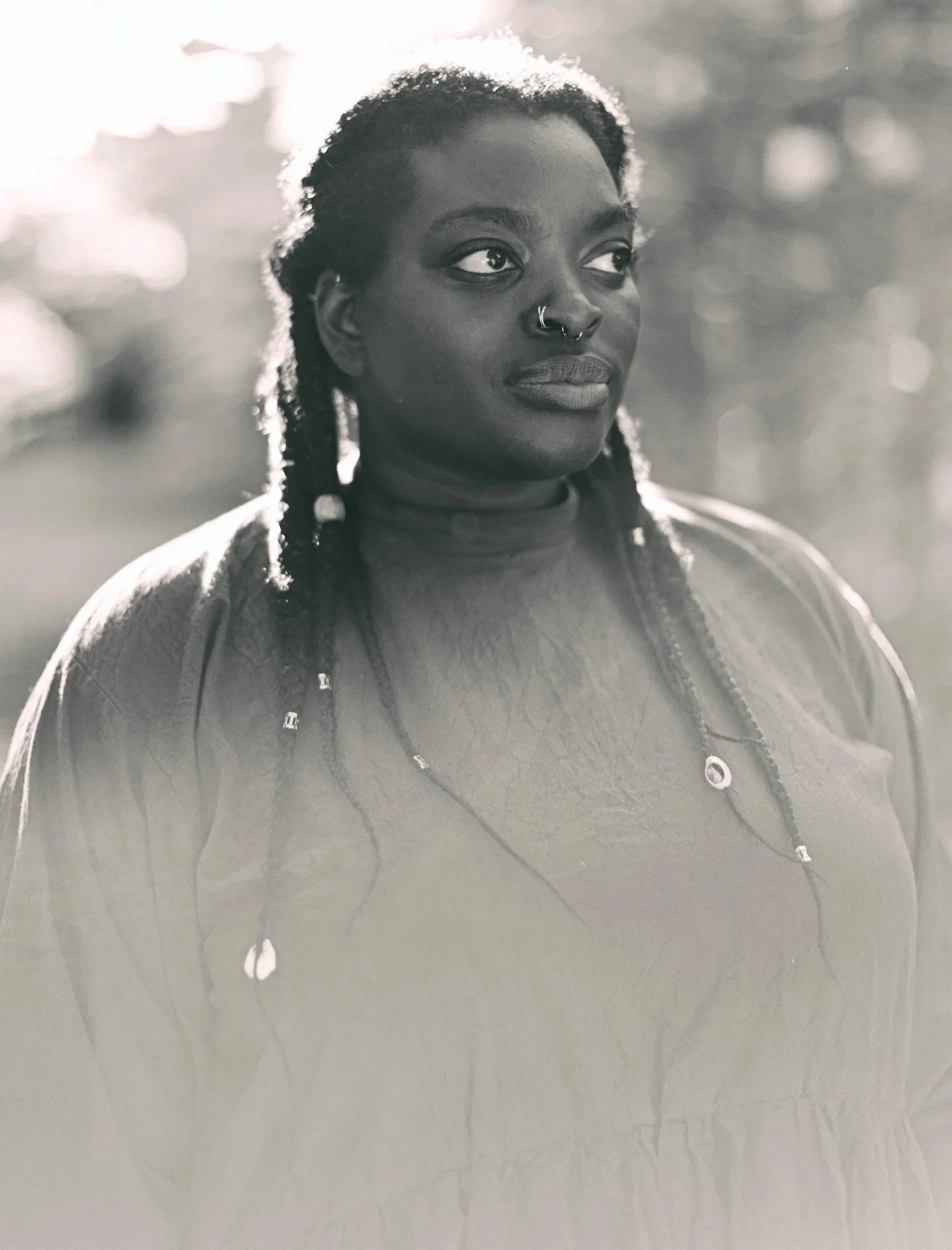 Black woman with braided hair, wearing nose rings, looking to her right in a black and white photo.
