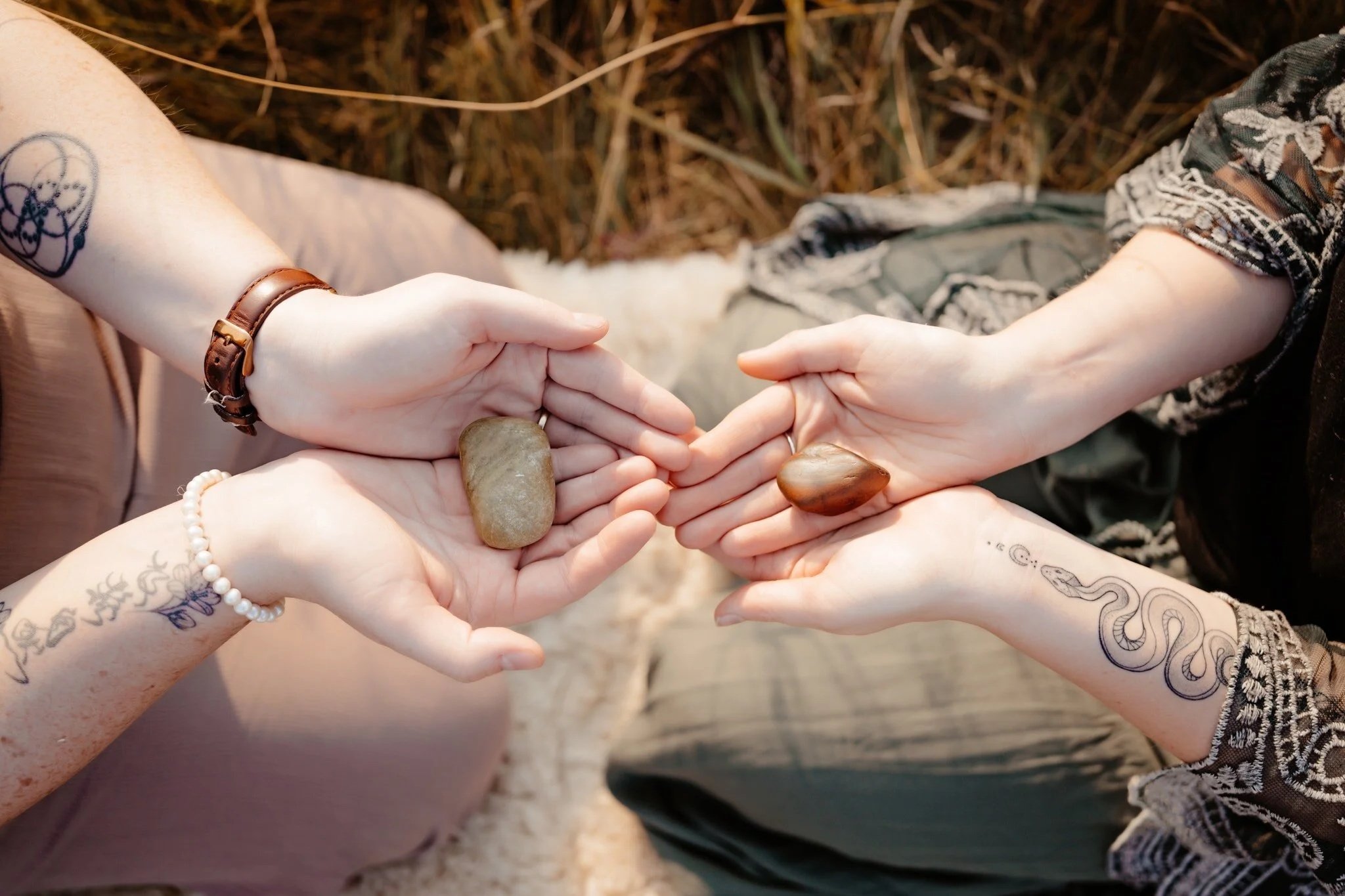 Four hands holding stones together outdoors with grassy background.