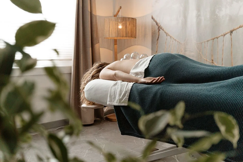 A person lying on their side on a bed, partially covered with a blanket in a cozy bedroom setting.