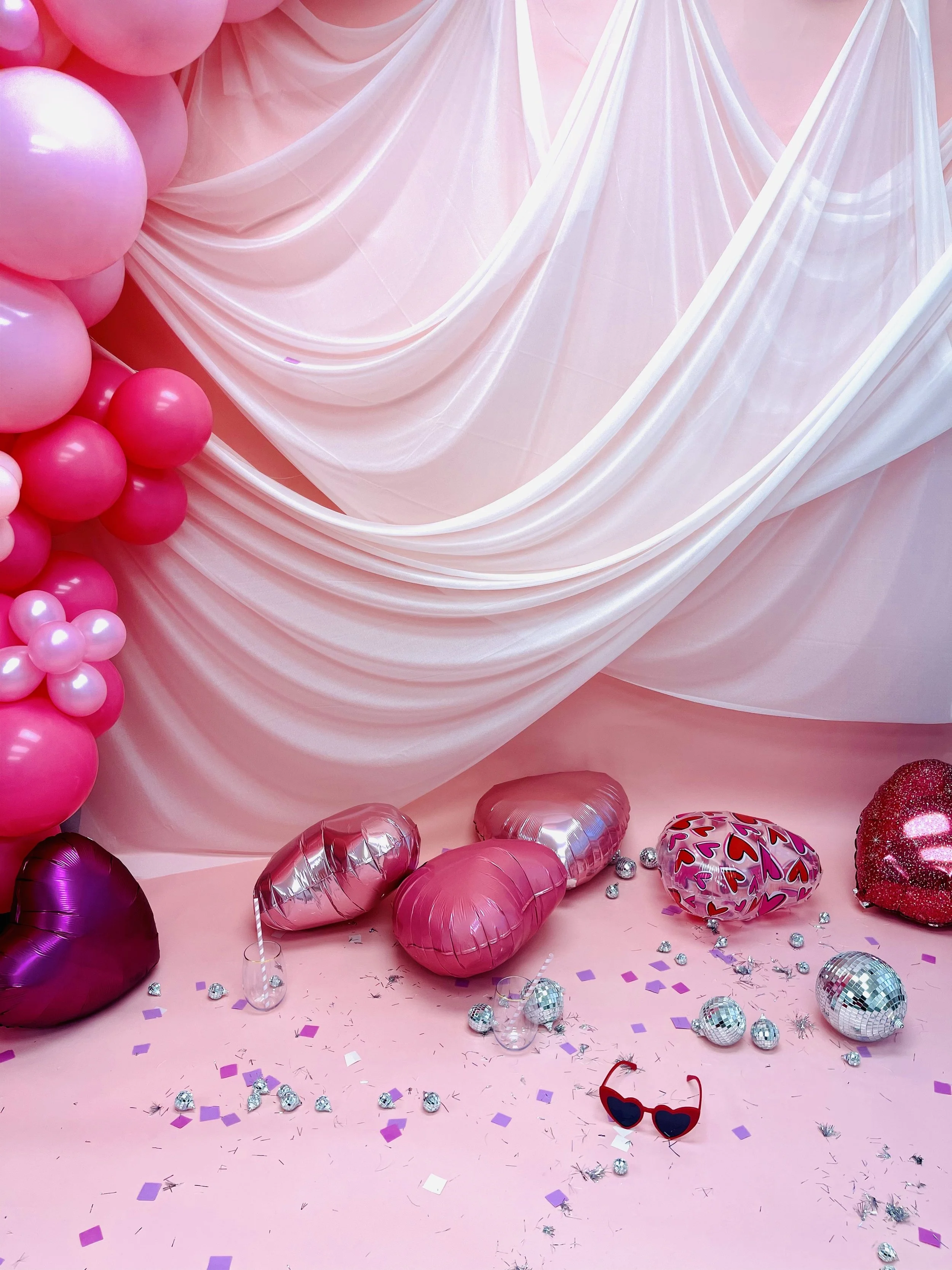 Pink drapery backdrop with heart-shaped foil balloons for a Valentine's photo setup
