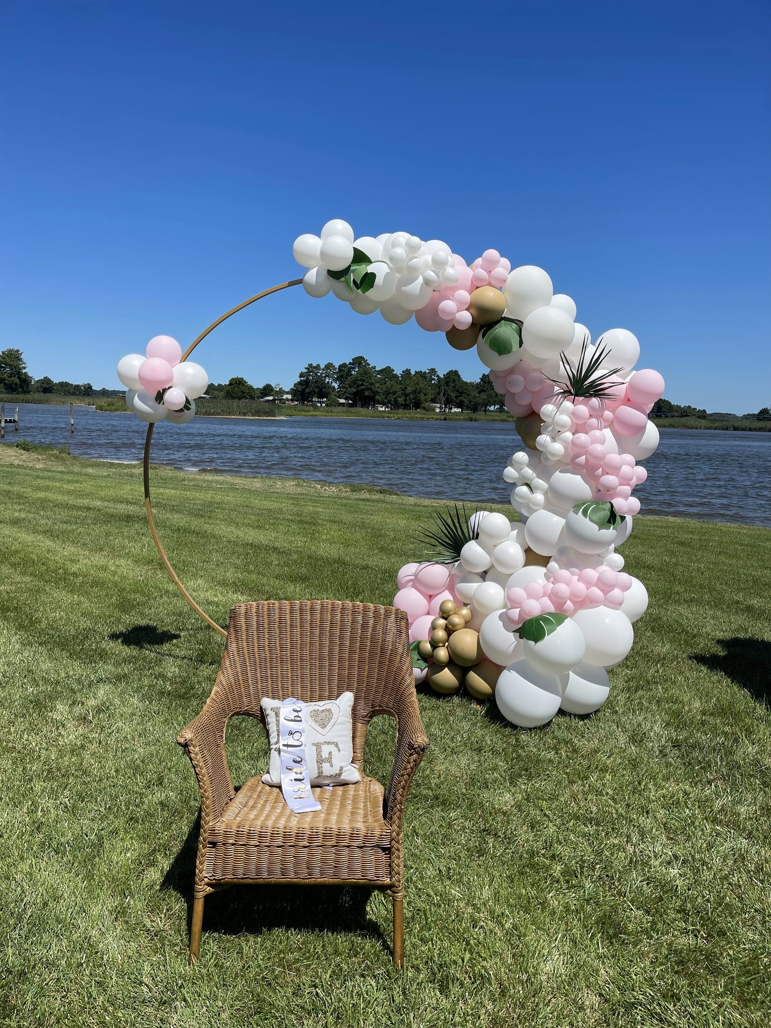 Pink, white, and gold balloon arch by a lakeside for a bridal shower photo backdrop