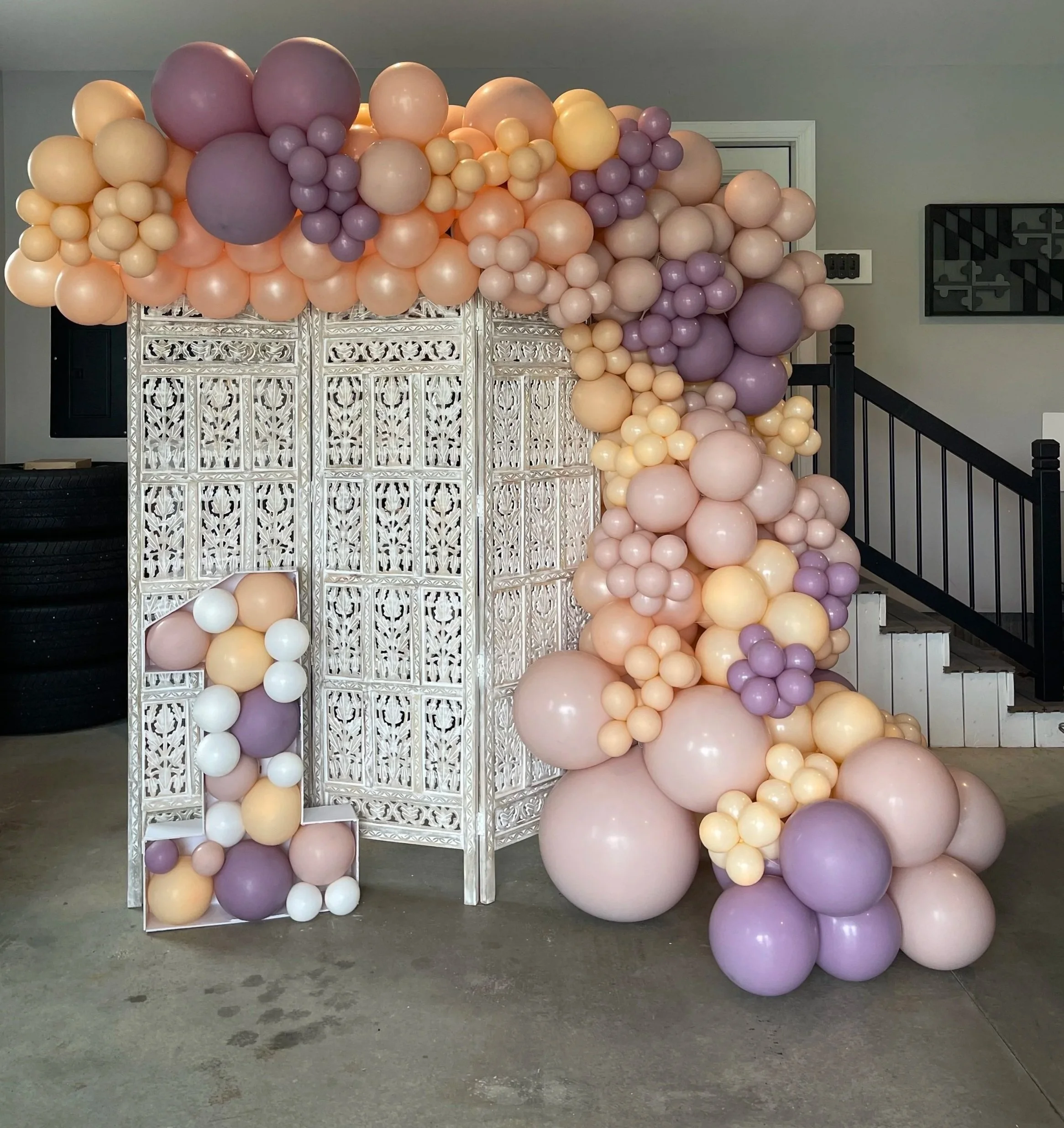 Mauve, blush, and peach balloon garland on a decorative screen backdrop for a first birthday party