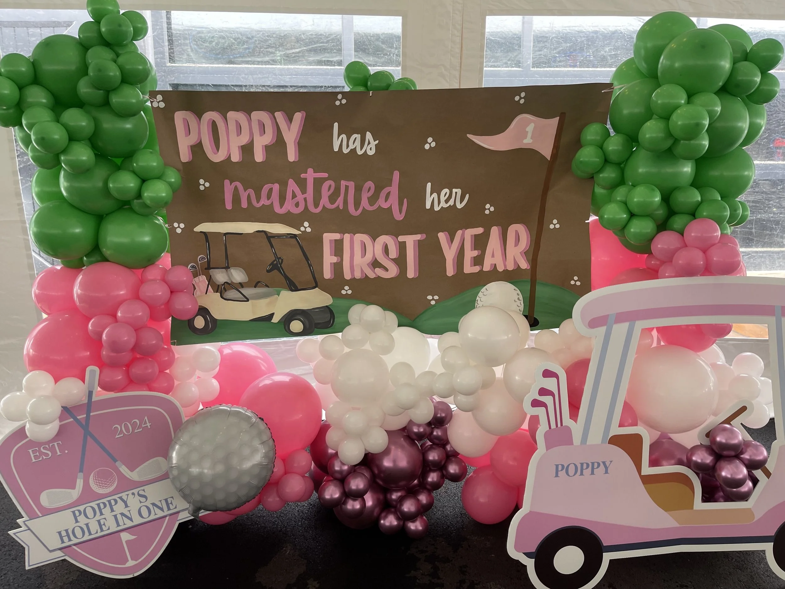 Golf-themed first birthday balloon display with pink, green, and burgundy balloons for Poppy's party