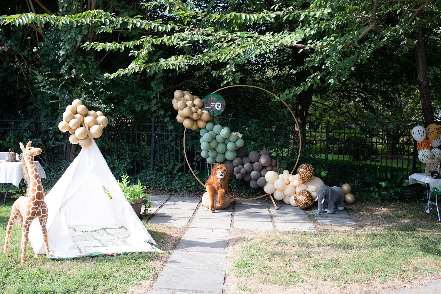 Safari-themed birthday backdrop with balloon hoop, plush jungle animals, and teepee tent for Leo's party
