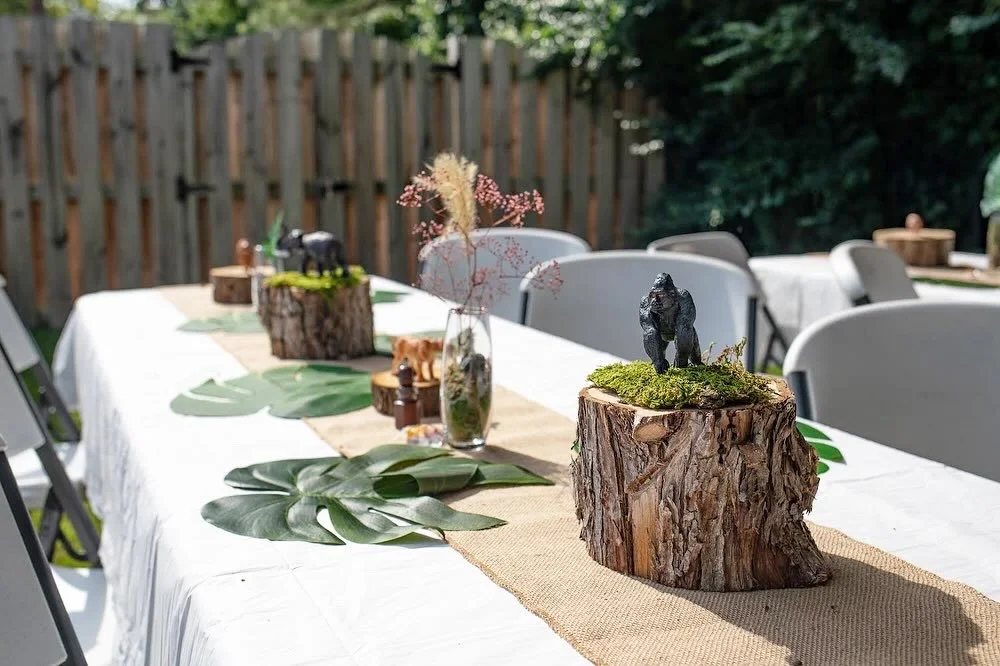 Outdoor safari-themed table setting with tree stump centerpieces and tropical leaf runners