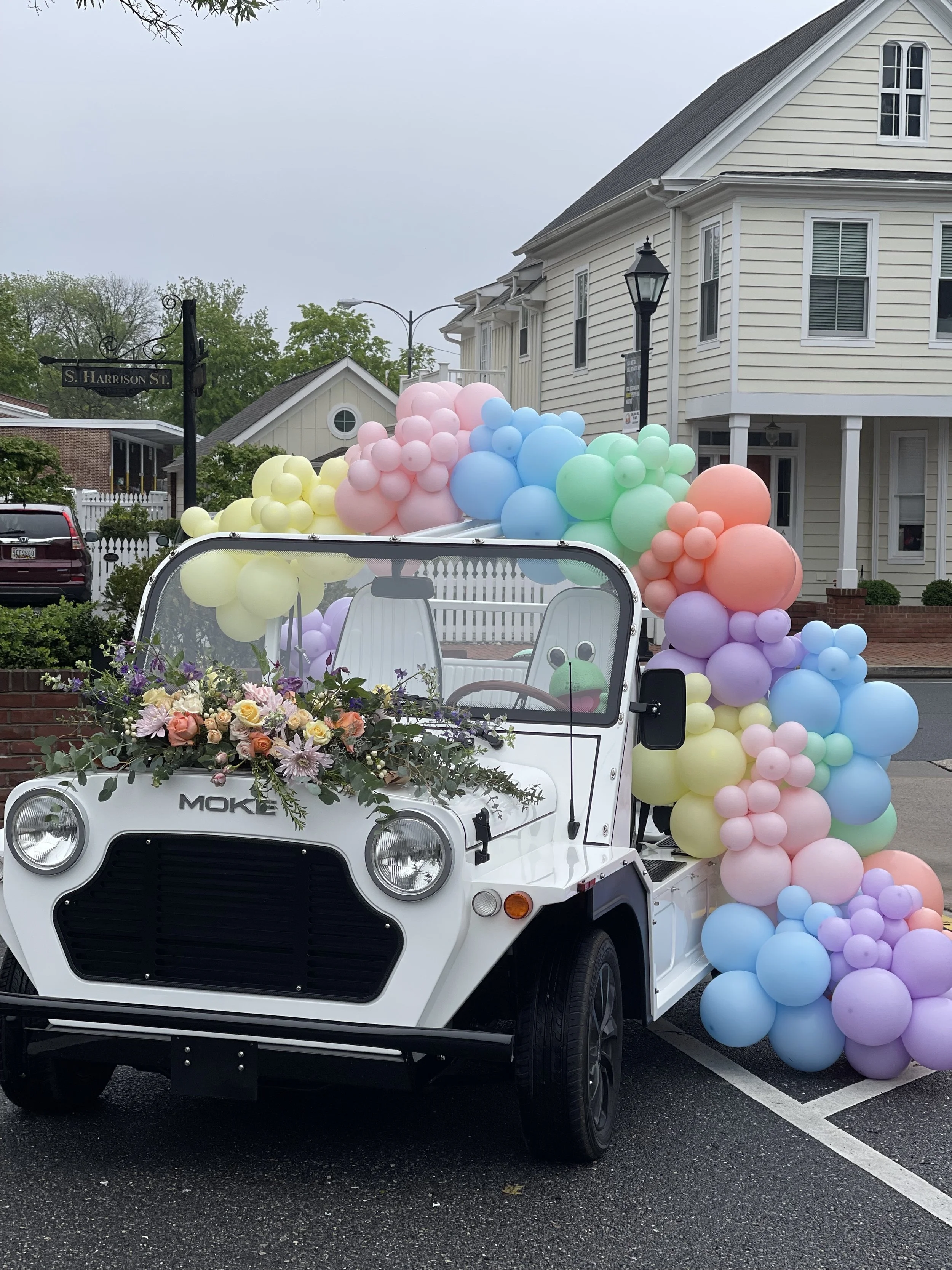 Pastel rainbow balloon garland and fresh florals decorating a vintage Moke car for a special event