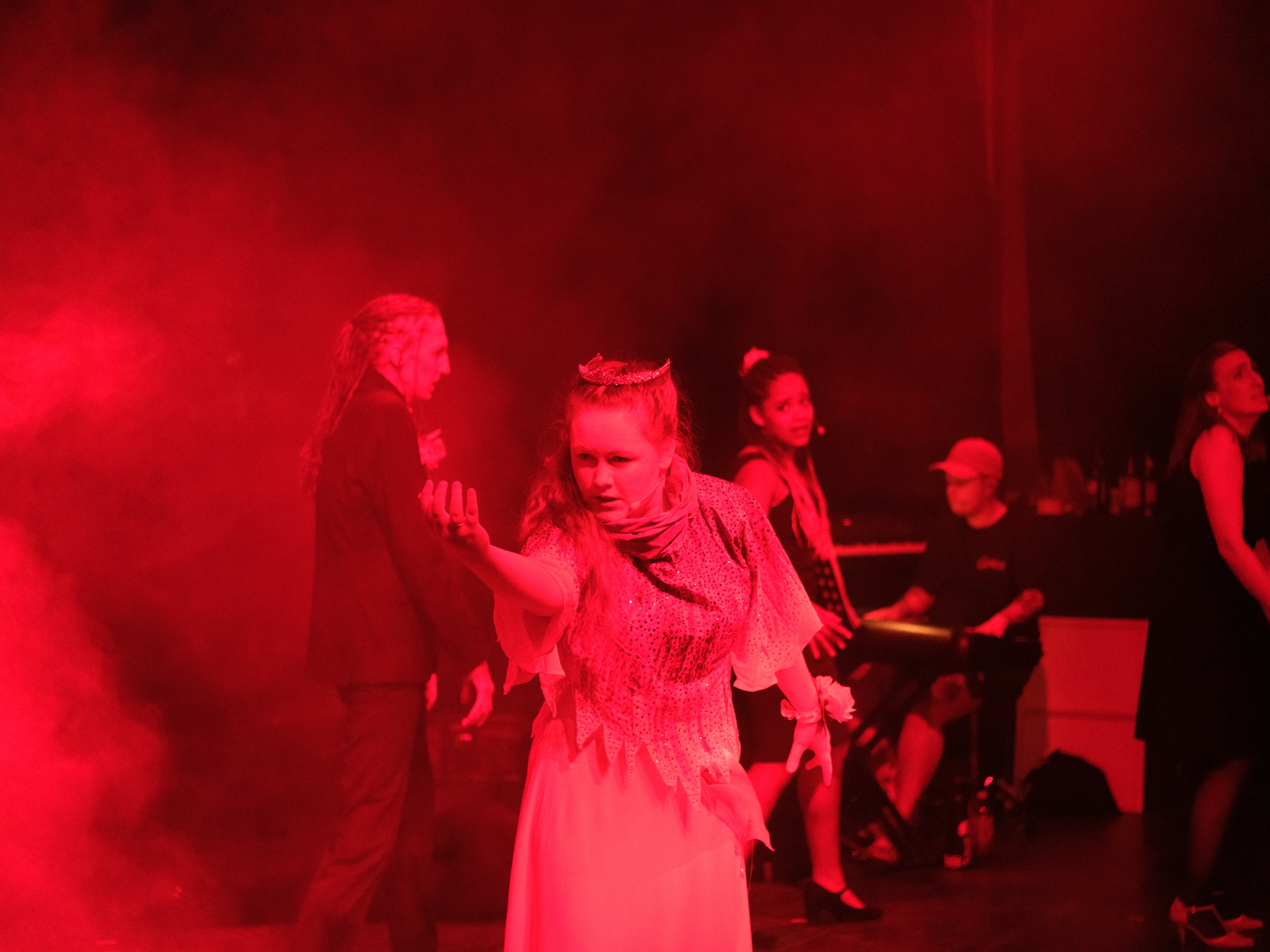 Mehrere Darsteller:innen auf einer Bühne, beleuchtet von rotem Licht, in Kostümen. Endszene von Carrie – das Musical