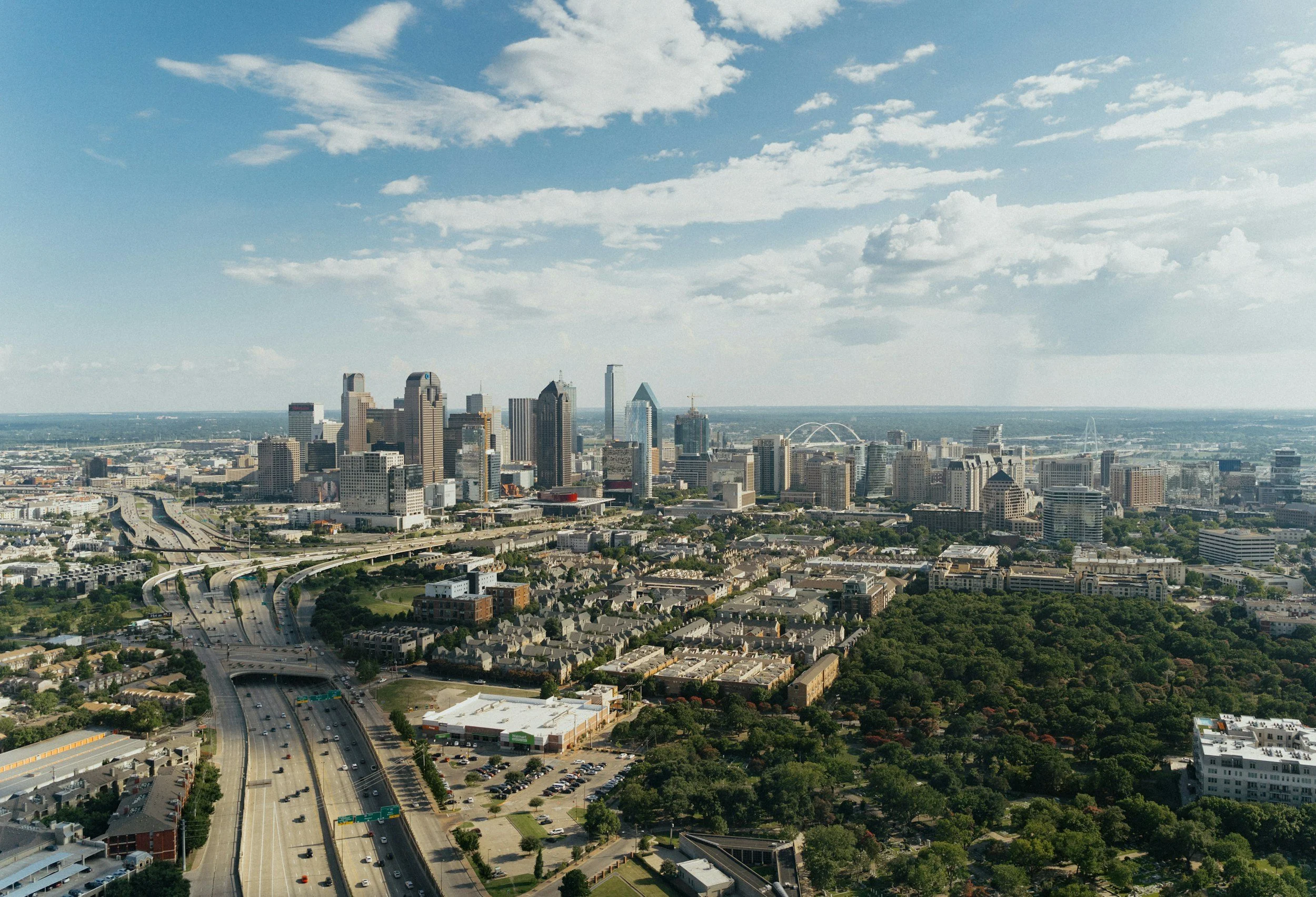 A city skyline with tall skyscrapers, highways, and residential areas under a partly cloudy sky.