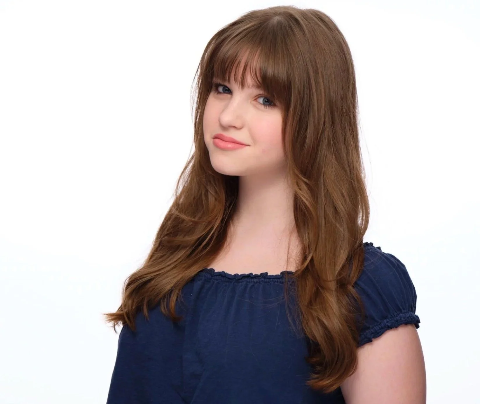 Portrait of a young woman with long, wavy brown hair wearing a navy blue top, posing against a white background.