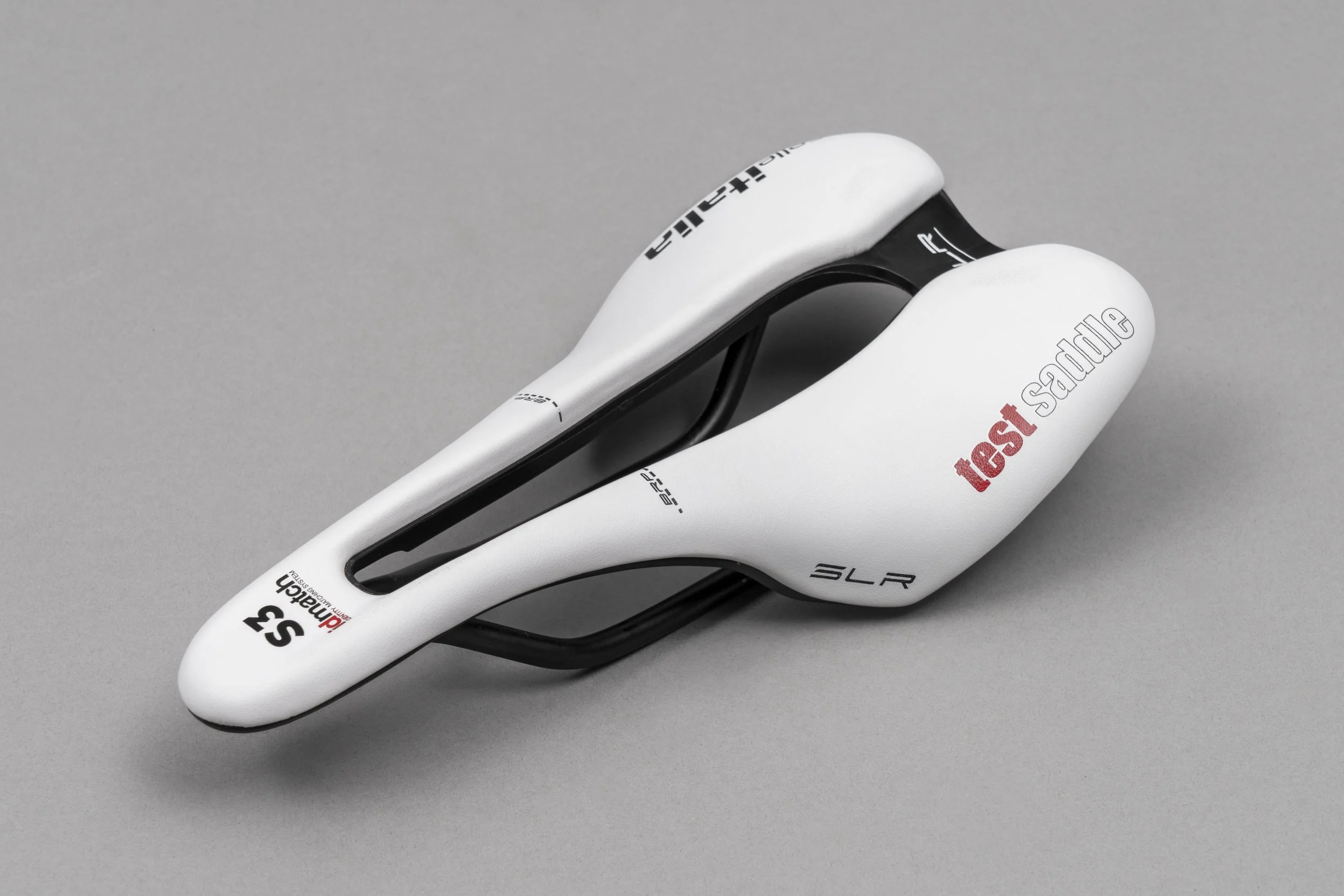 Close-up of a white Specialized S-Works Tarmac SL7 road bicycle saddle with black accents and red and black branding, on a gray background.