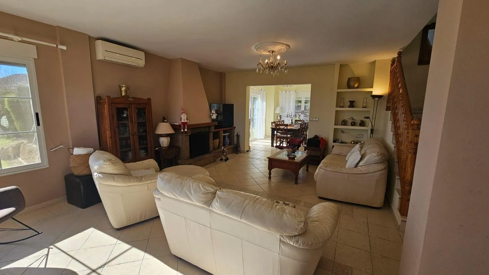 Sala de estar con sillones blancos, chimenea, estantería y ventana. Comedor al fondo y puerta corrediza que lleva a un patio exterior.