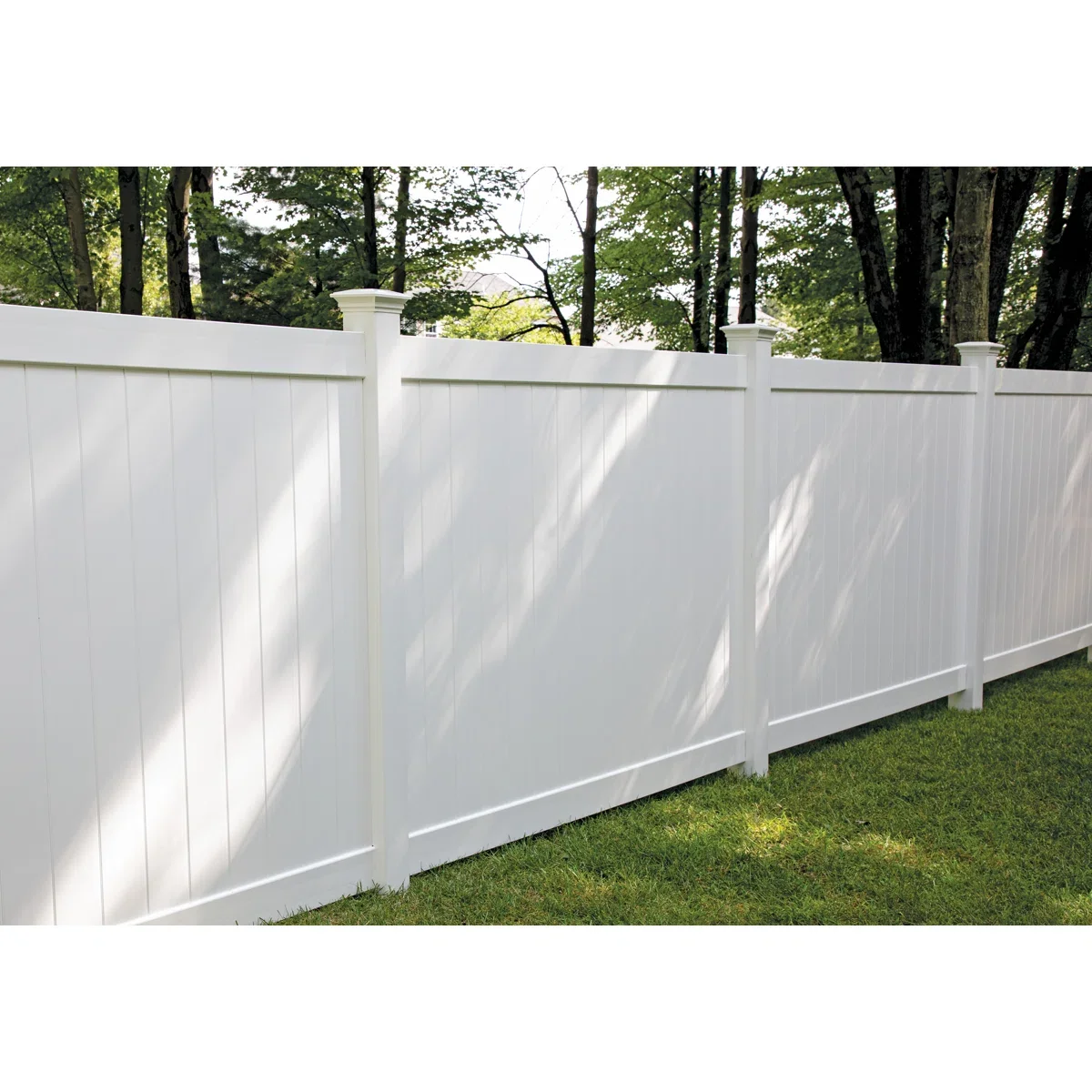 White privacy fence with vertical panels and decorative posts in a grassy backyard with trees in the background.